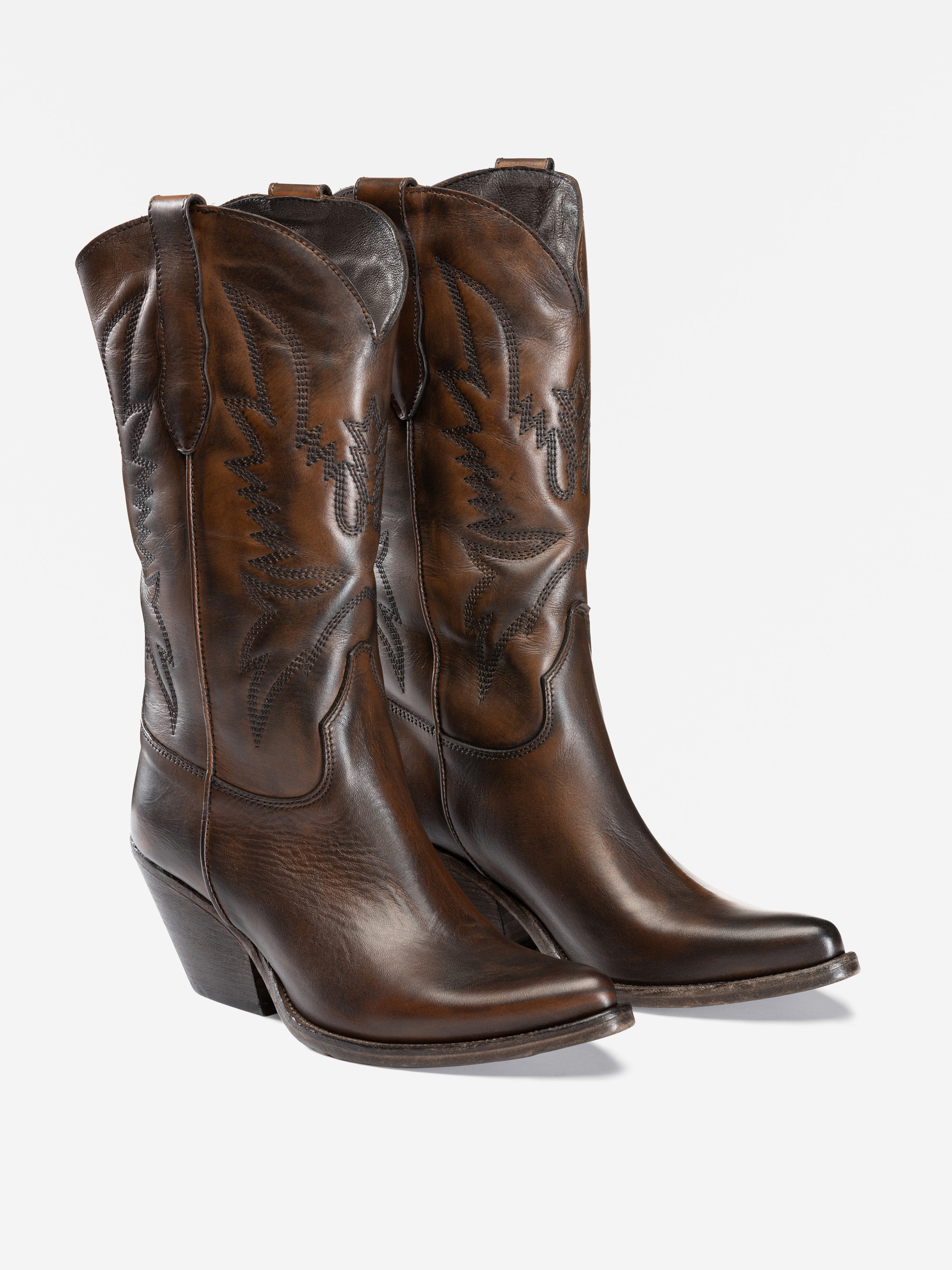 Ein Paar Cowboystiefel aus braunem Leder mit Ziernähten, abgewinkelten Absätzen und spitzen Zehen, dargestellt vor einem schlichten weißen Hintergrund.