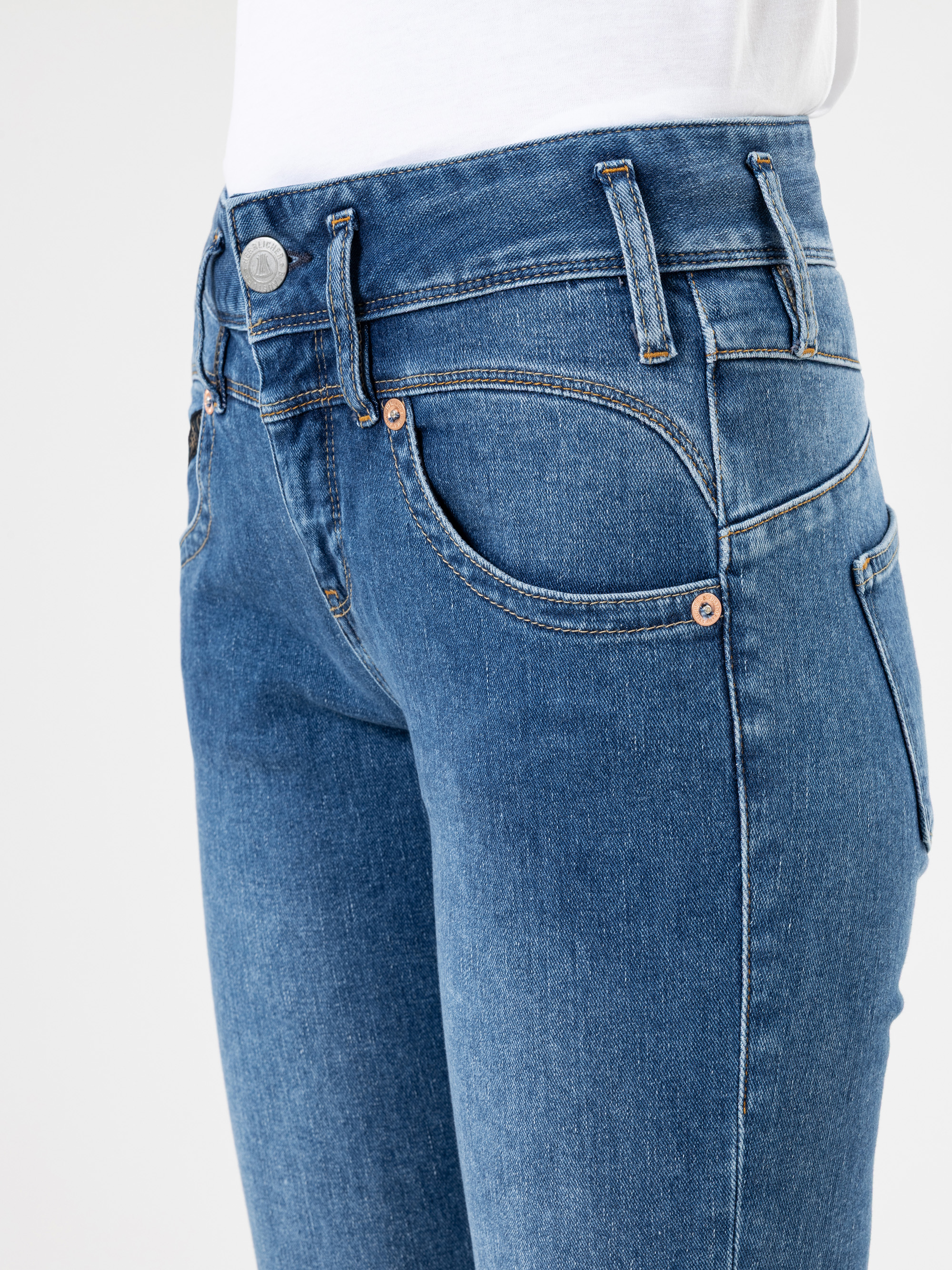 Nahaufnahme einer Person, die eine blaue Jeans und ein weißes Oberteil trägt. Sie zeigt die Vorder- und Seitenansicht der Jeans mit sichtbaren Taschen, Gürtelschlaufen und Nahtdetails.