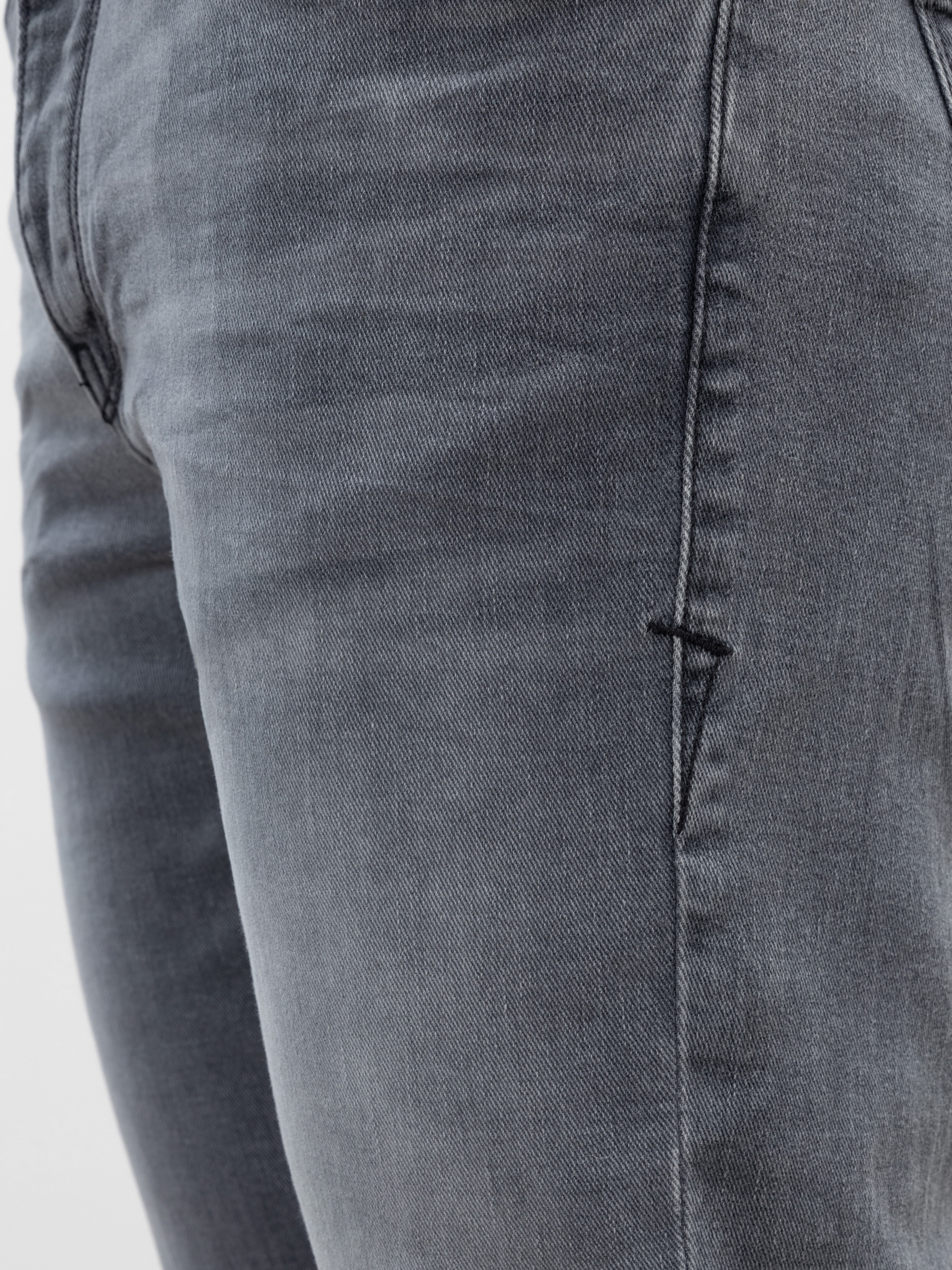 Nahaufnahme einer Person, die eine verblichene graue Denim-Jeans trägt, die die Vordertasche und den Oberschenkelbereich zeigt. Die Nähte und die Textur des Stoffes sind deutlich sichtbar.