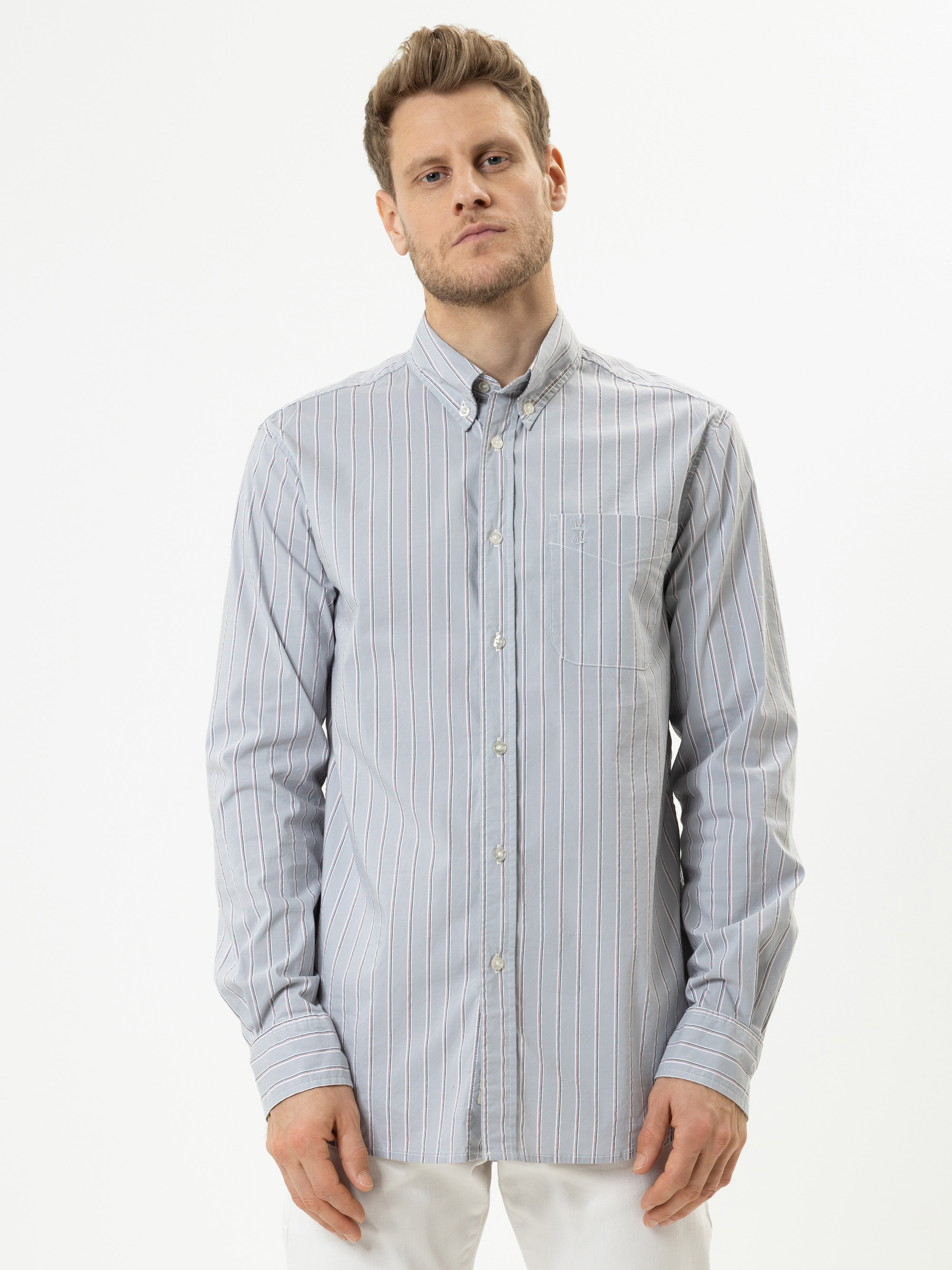 Ein Mann in einem hellblau-weiß vertikal gestreiften Hemd mit langen Ärmeln steht vor einem schlichten weißen Hintergrund.