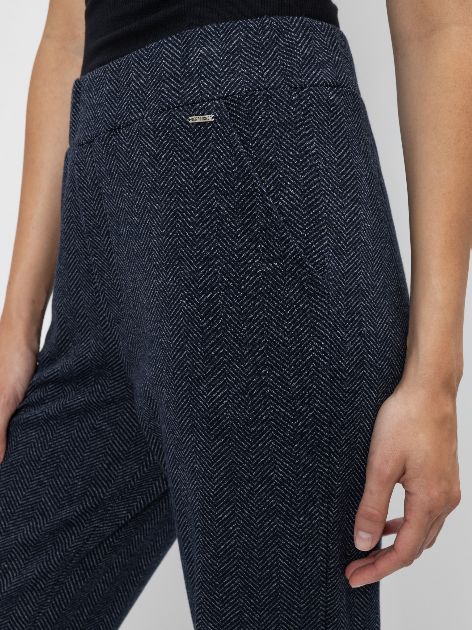 Eine Person, die eine marineblaue Hose mit hoher Taille und Fischgrätenmuster und einer Seitentasche trägt, steht mit einer entspannten Hand an der Seite. Das Bild ist am Oberkörper und in der Mitte des Oberschenkels abgeschnitten.