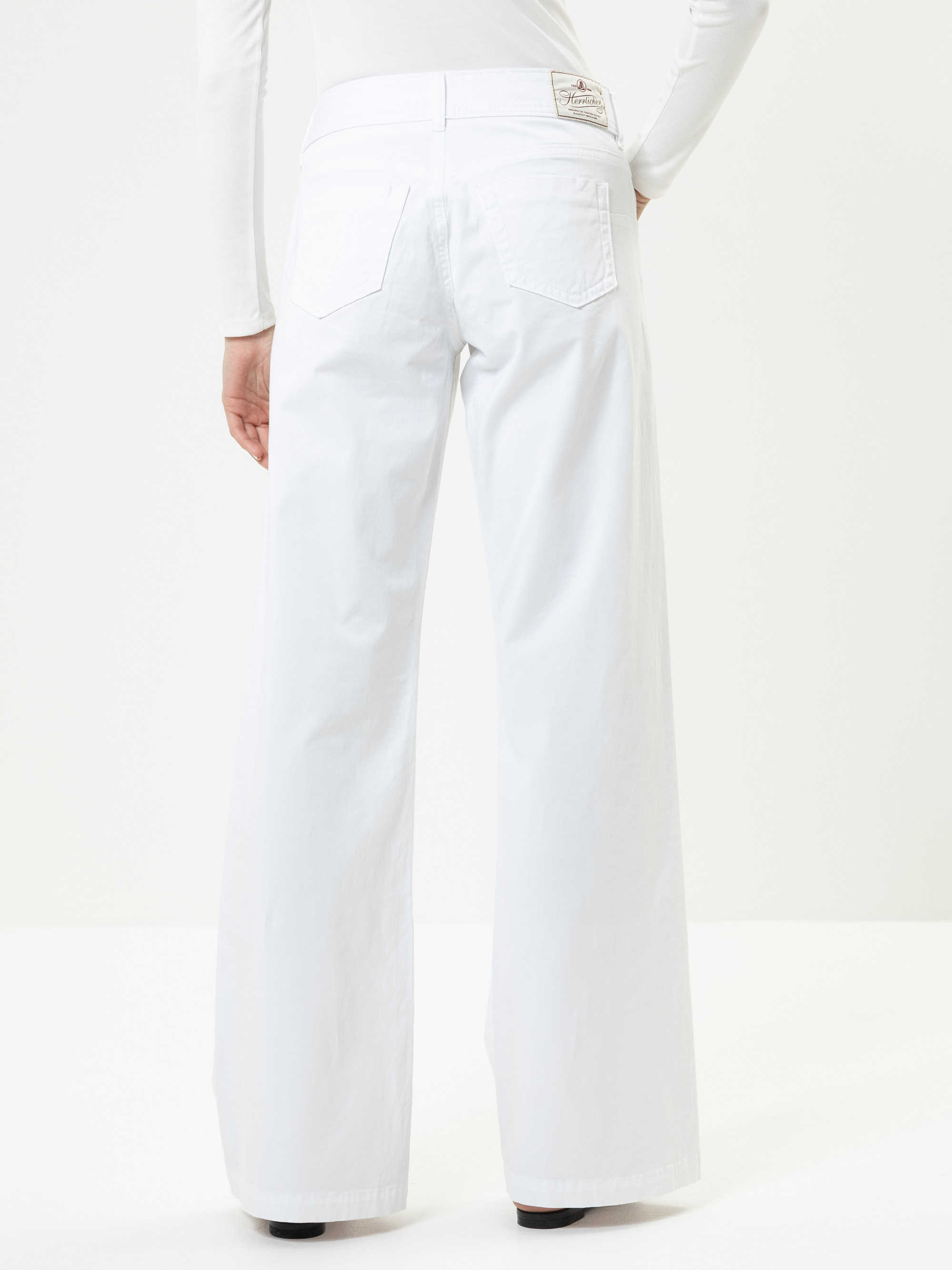 Person, die eine weiße Jeans mit hoher Taille und weitem Bein und ein weißes langärmeliges Oberteil trägt, von hinten gesehen vor einem einfarbig weißen Hintergrund. Die Jeans hat zwei Gesäßtaschen und ein sichtbares Etikett am Bund.