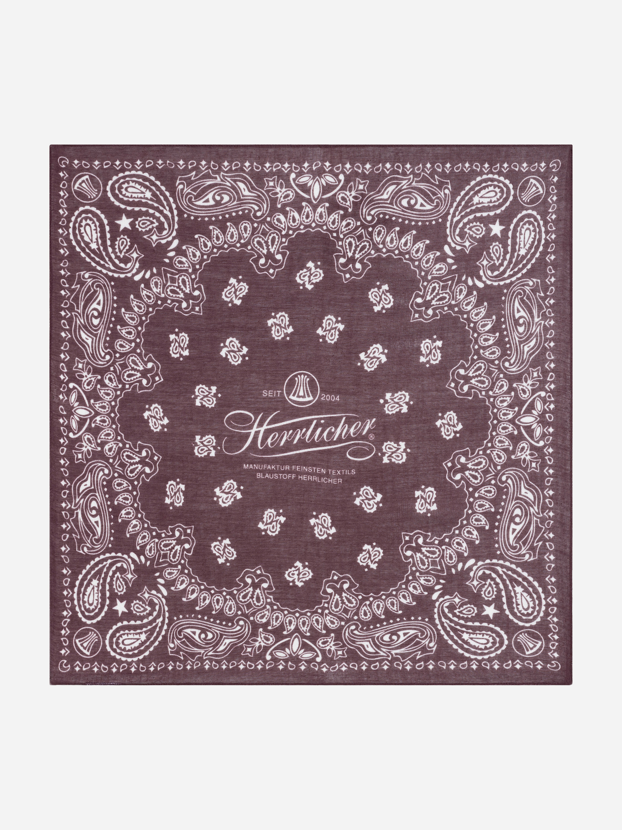 Ein quadratisches, dunkelviolettes Bandana mit einem weißen Paisley-Muster am Rand und einem Logo in der Mitte mit der Aufschrift „Herrlicher“, darunter der Text „SEIT 2004“ sowie „MANUFAKTUR FEINSTEN TEXTILS BLAUSTOFF HERRLICHER“ auf einem e