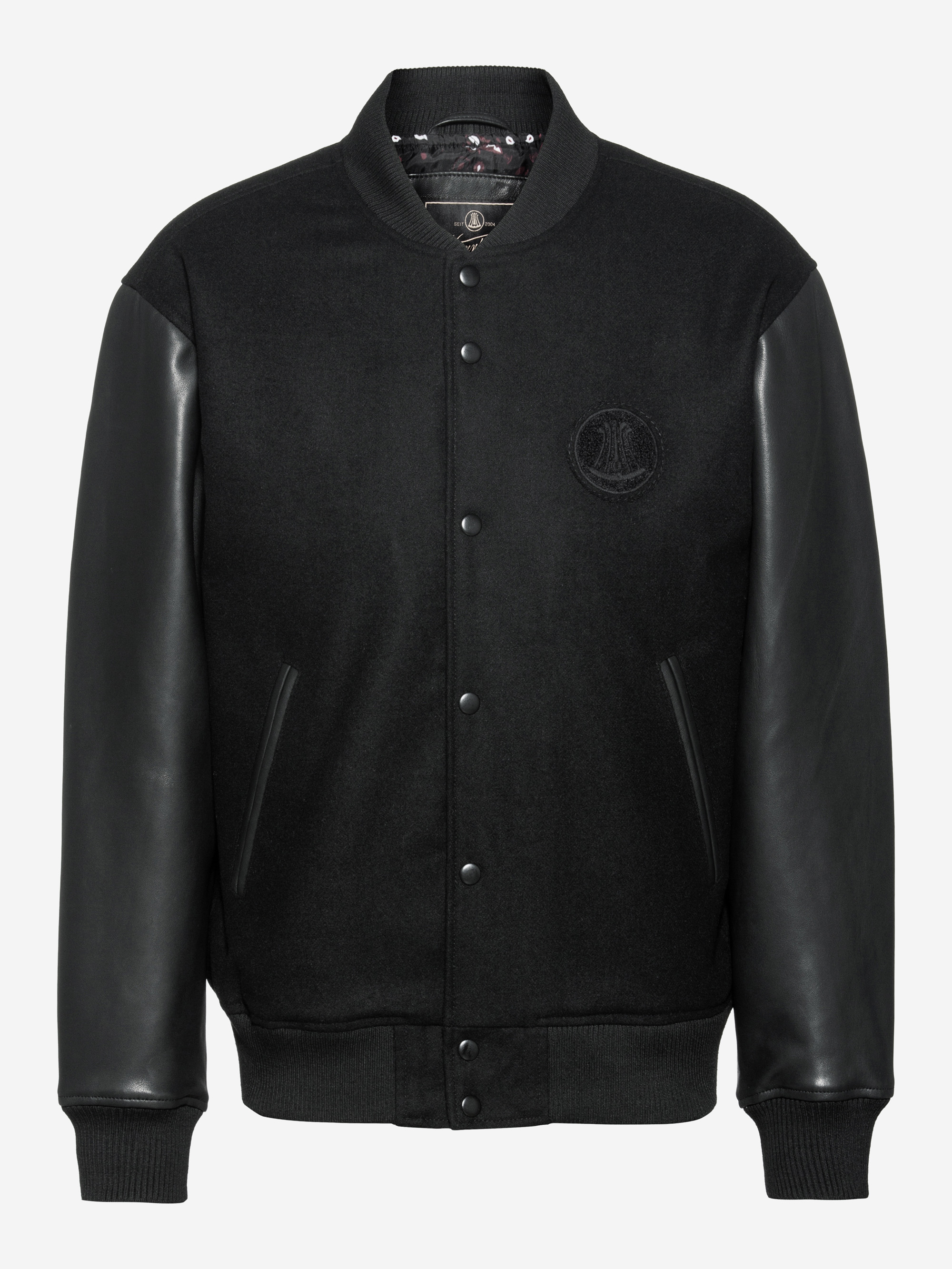 Schwarze Uniformjacke mit Lederärmeln, geripptem Kragen, Manschetten und Saum, Druckknopfverschluss vorne und zwei schrägen Seitentaschen. Der Körper ist aus einem matten Stoff gefertigt, während die Ärmel ein glänzendes Leder-Finish haben.