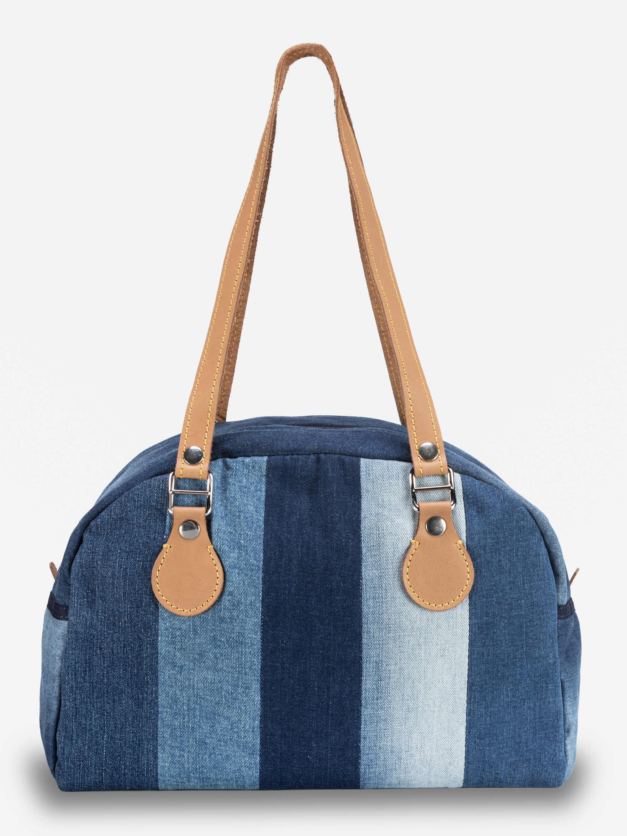Eine Handtasche mit vertikalen jeansblauen Streifen in verschiedenen Schattierungen, mit hellbraunen Ledergriffen und silbernen Beschlägen vor einem schlichten weißen Hintergrund.