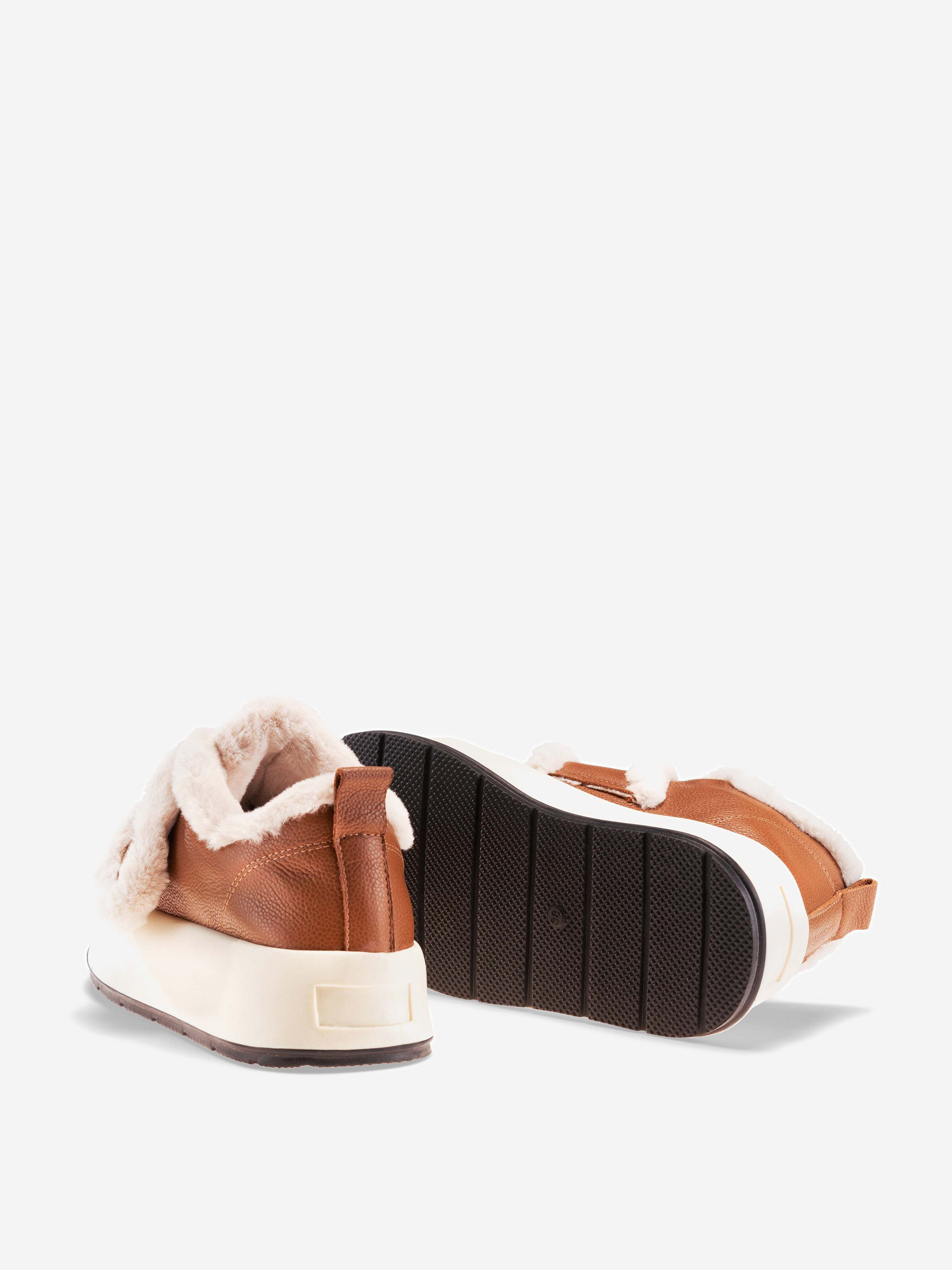 Ein Paar braune Slipper mit weißer Sohle und weichem, cremefarbenem Kunstpelzfutter, dargestellt von hinten und von der Seite auf weißem Hintergrund.