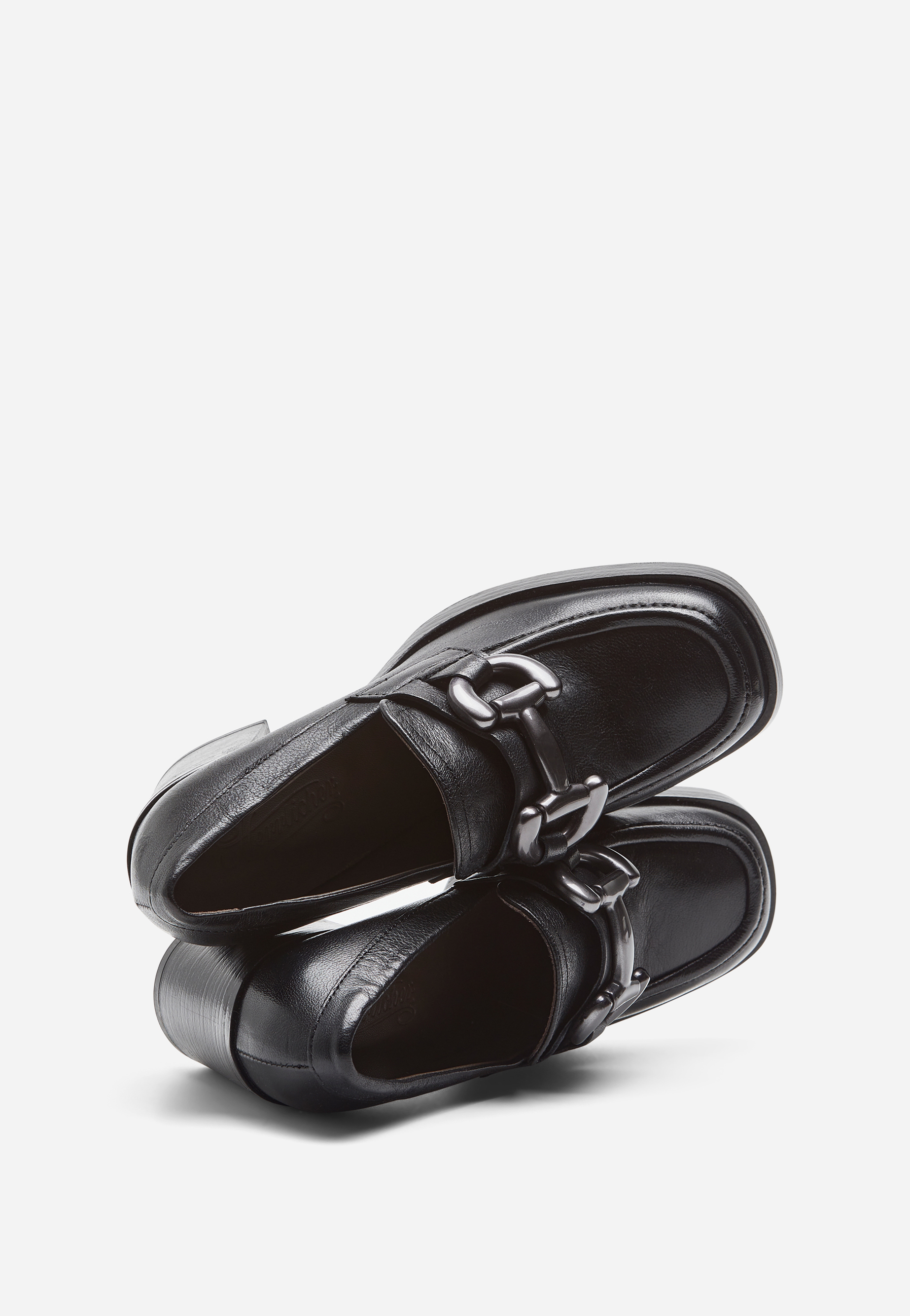 Ein Paar schwarze Lederslipper mit klobigen Metallkettchen auf der Vorderseite, die vor einem weißen Hintergrund übereinander angeordnet sind.