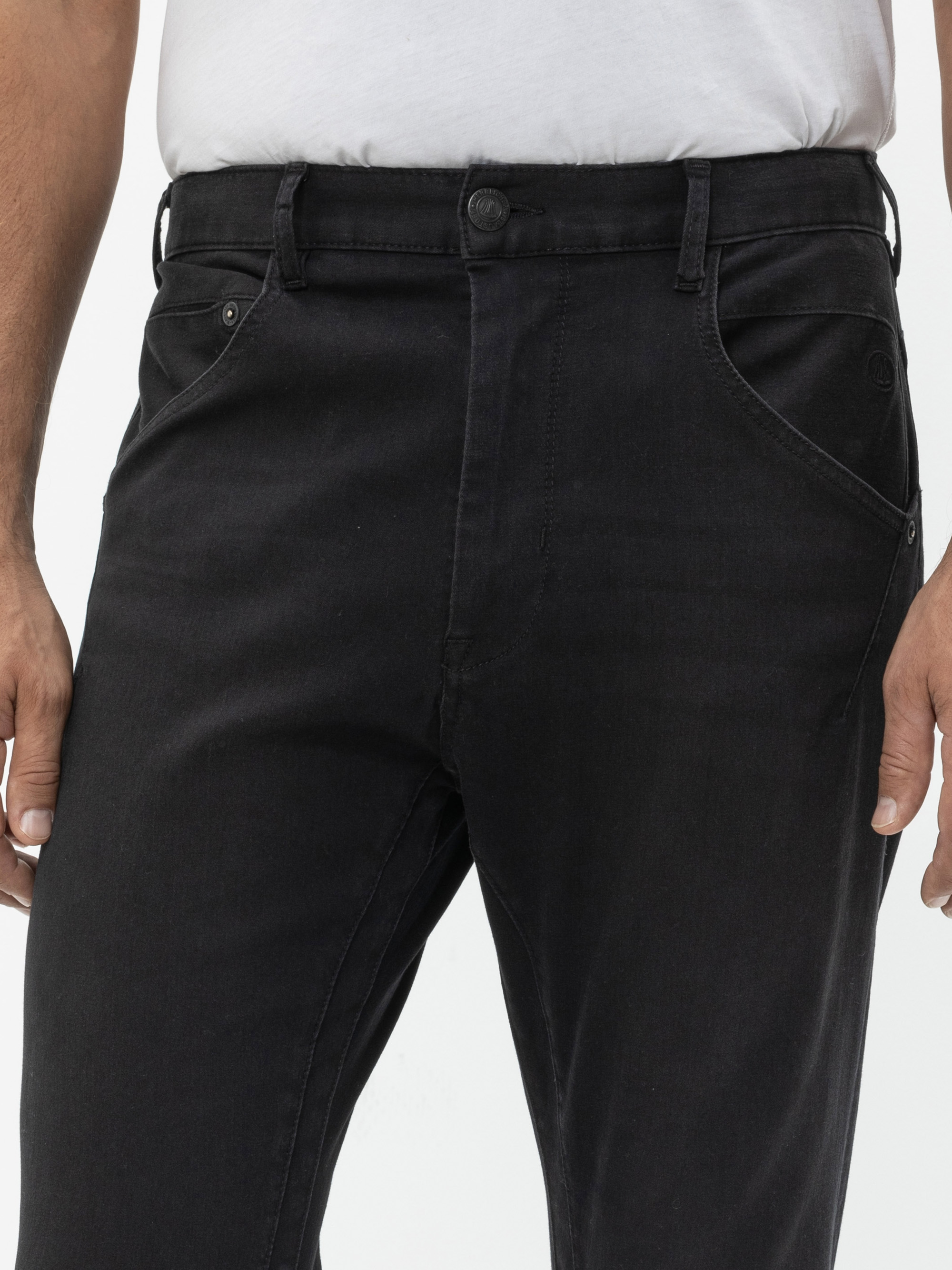 Eine Person, die ein einfaches weißes T-Shirt und eine schwarze Jeans trägt und eine Hand an die Seite legt, wird von der Taille bis zur Mitte des Oberschenkels vor einem weißen Hintergrund gezeigt.