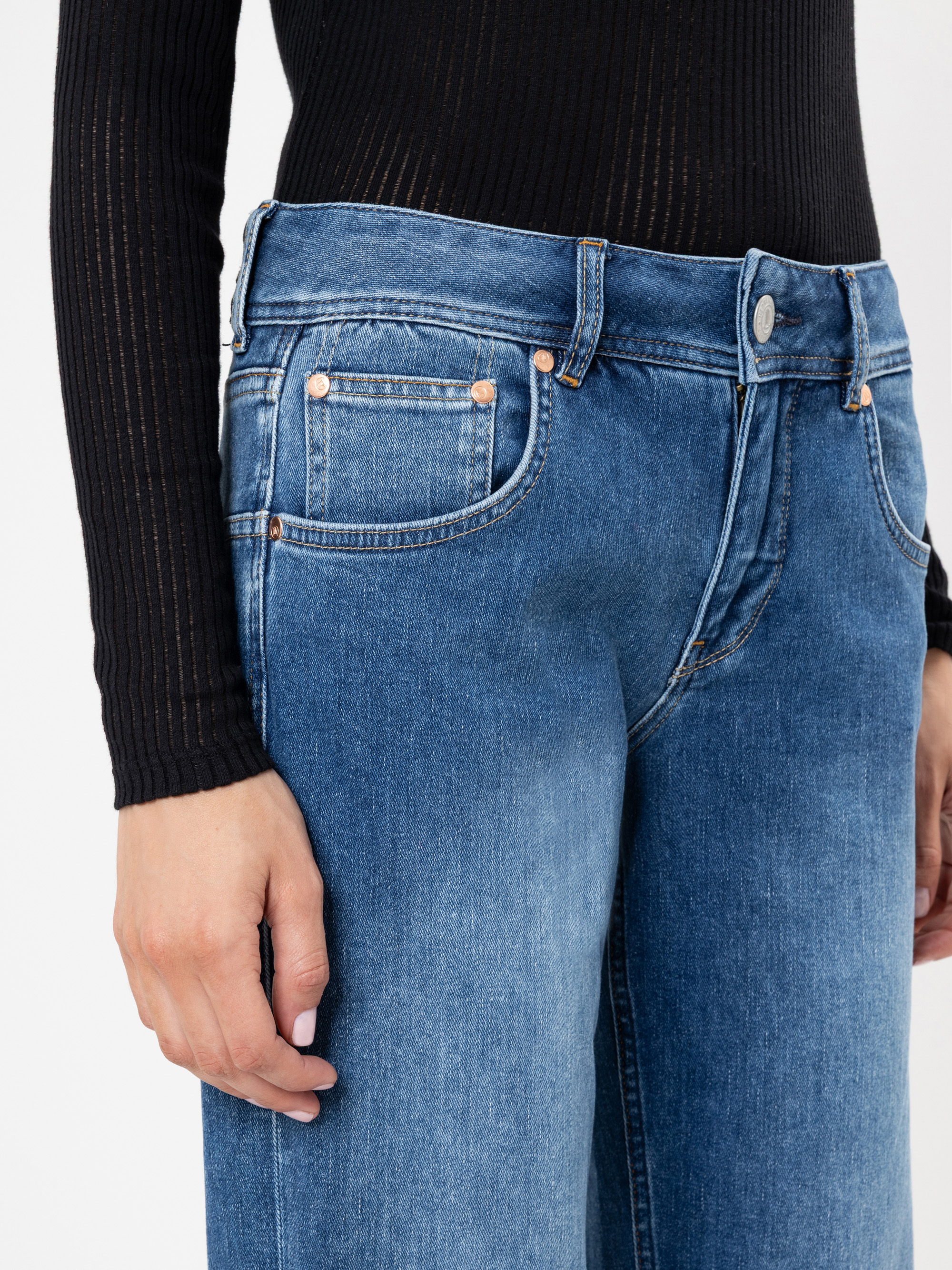 Eine Person trägt eine blaue Jeans mit hoher Taille und ein langärmeliges schwarzes geripptes Oberteil, das von der Taille bis zur Mitte des Oberschenkels reicht, wobei ein Arm locker an der Seite liegt.