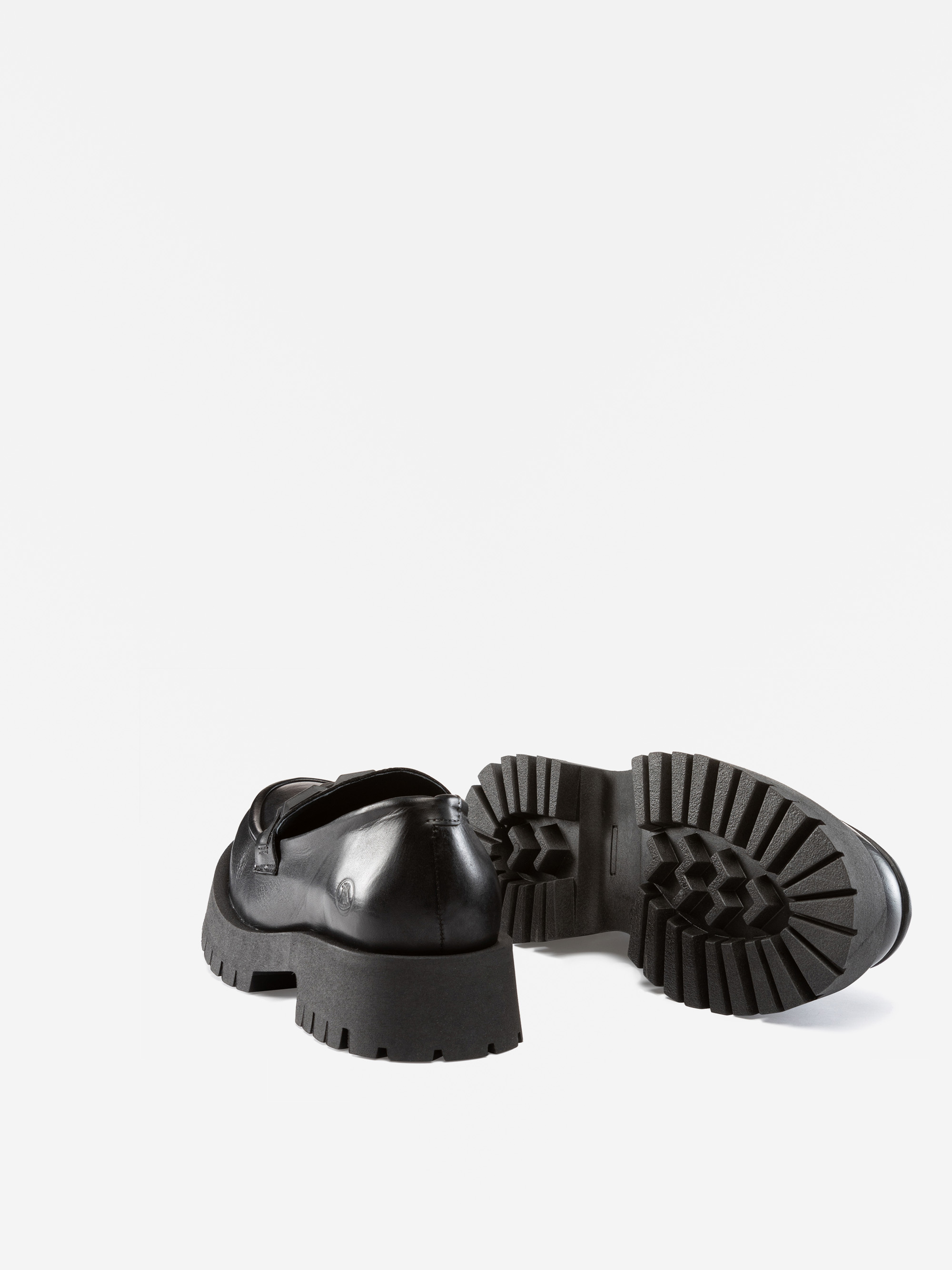 Ein Paar schwarzer, klobiger Slipper, von denen einer aufrecht steht und der andere auf der Seite liegt und die dicke, geriffelte Sohle vor einem schlichten weißen Hintergrund zeigt.