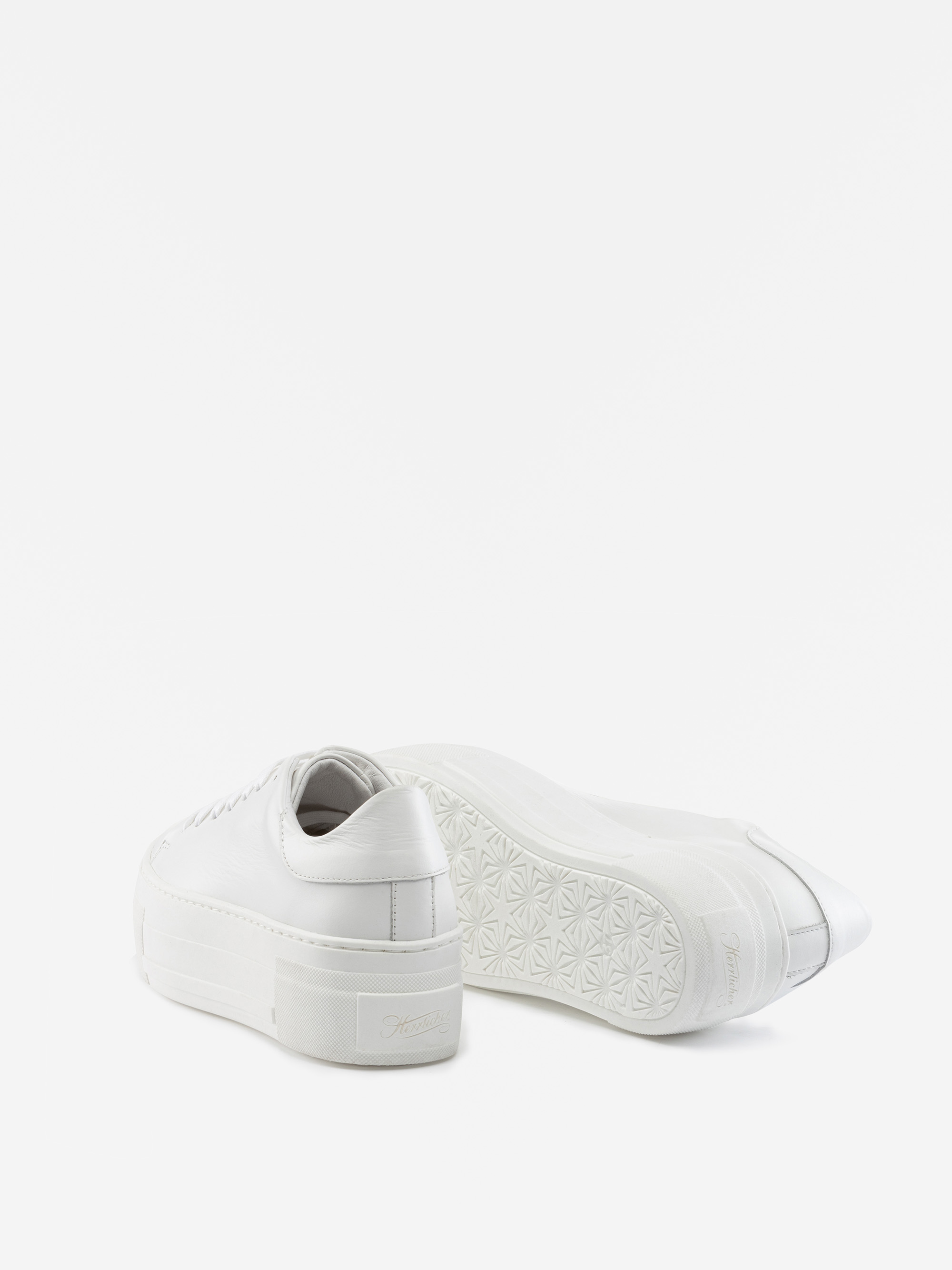 Ein Paar weißer Plateau-Sneakers, von denen einer aufrecht steht und der andere auf der Seite liegt und das strukturierte Sohlenmuster auf einem schlichten weißen Hintergrund zeigt.