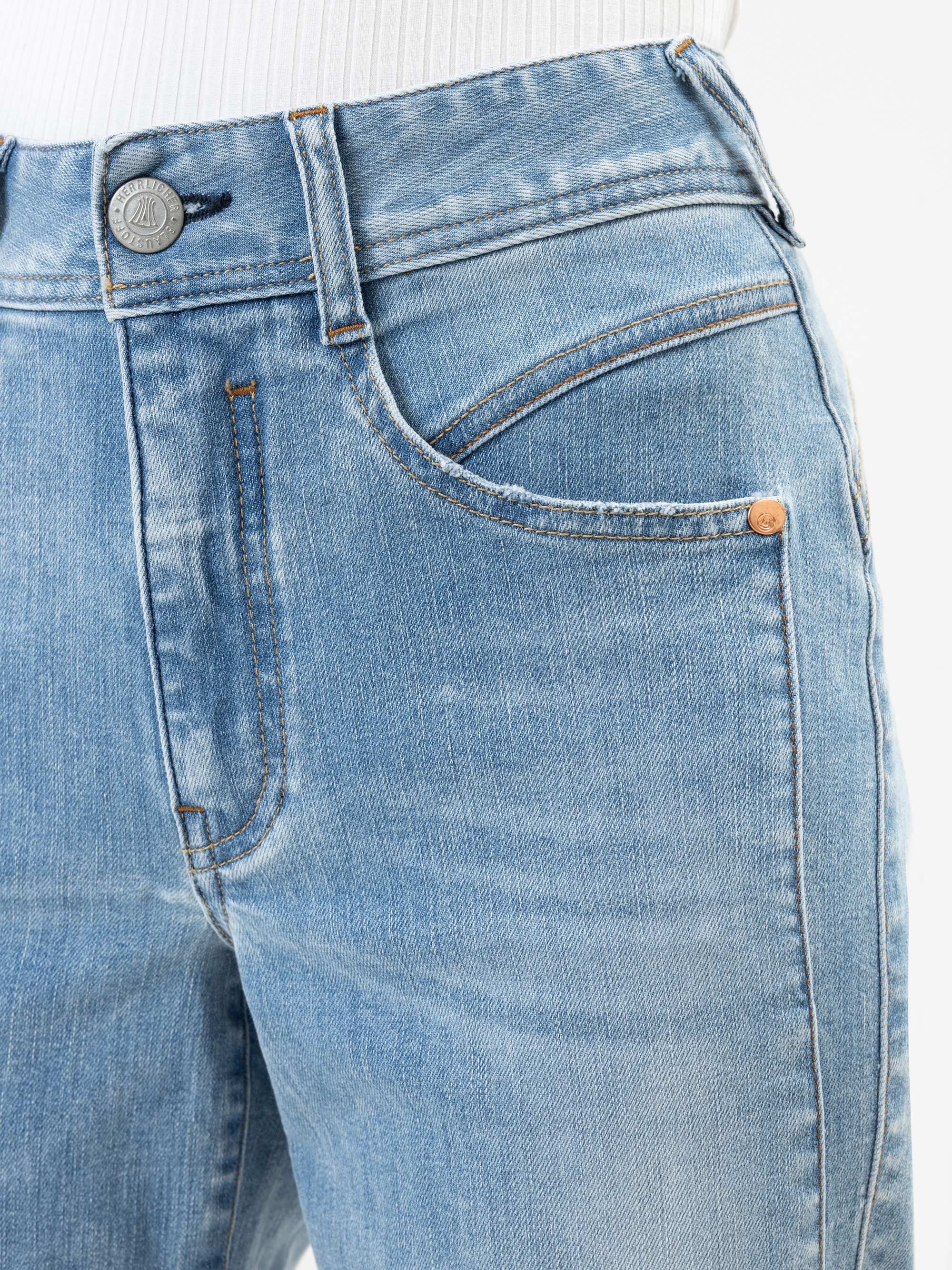 Nahaufnahme einer Person, die eine hellblaue Jeans trägt, bei der eine Vordertasche, ein Knopf und Gürtelschlaufen sichtbar sind. Die Jeans wird mit einem weißen gerippten Oberteil kombiniert, das in die Hose gesteckt wird.