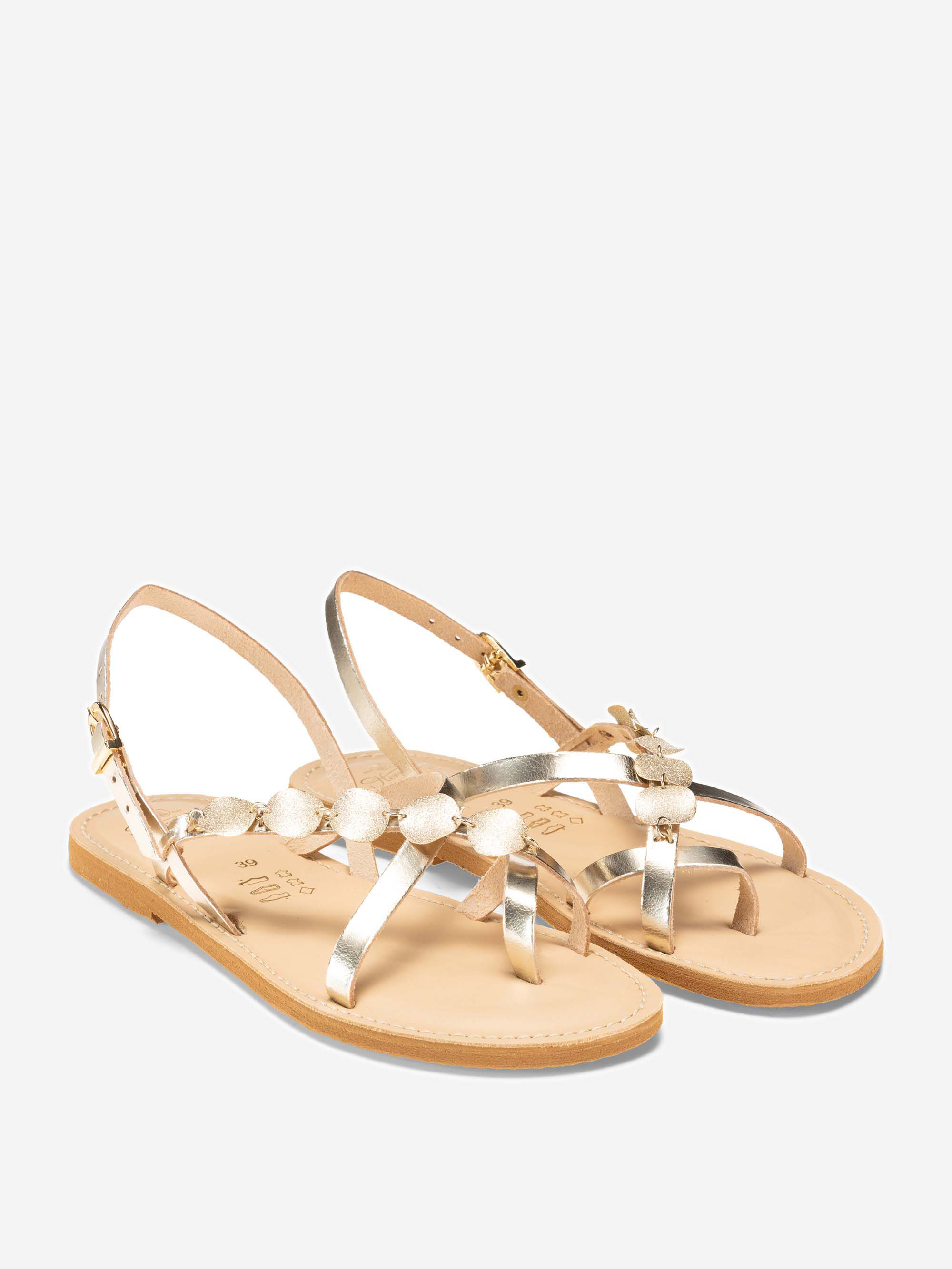 Ein Paar flache, hellbraune Ledersandalen mit goldenen Metallic-Riemen, kleinen runden Goldverzierungen und Knöchelschnallen auf weißem Hintergrund.