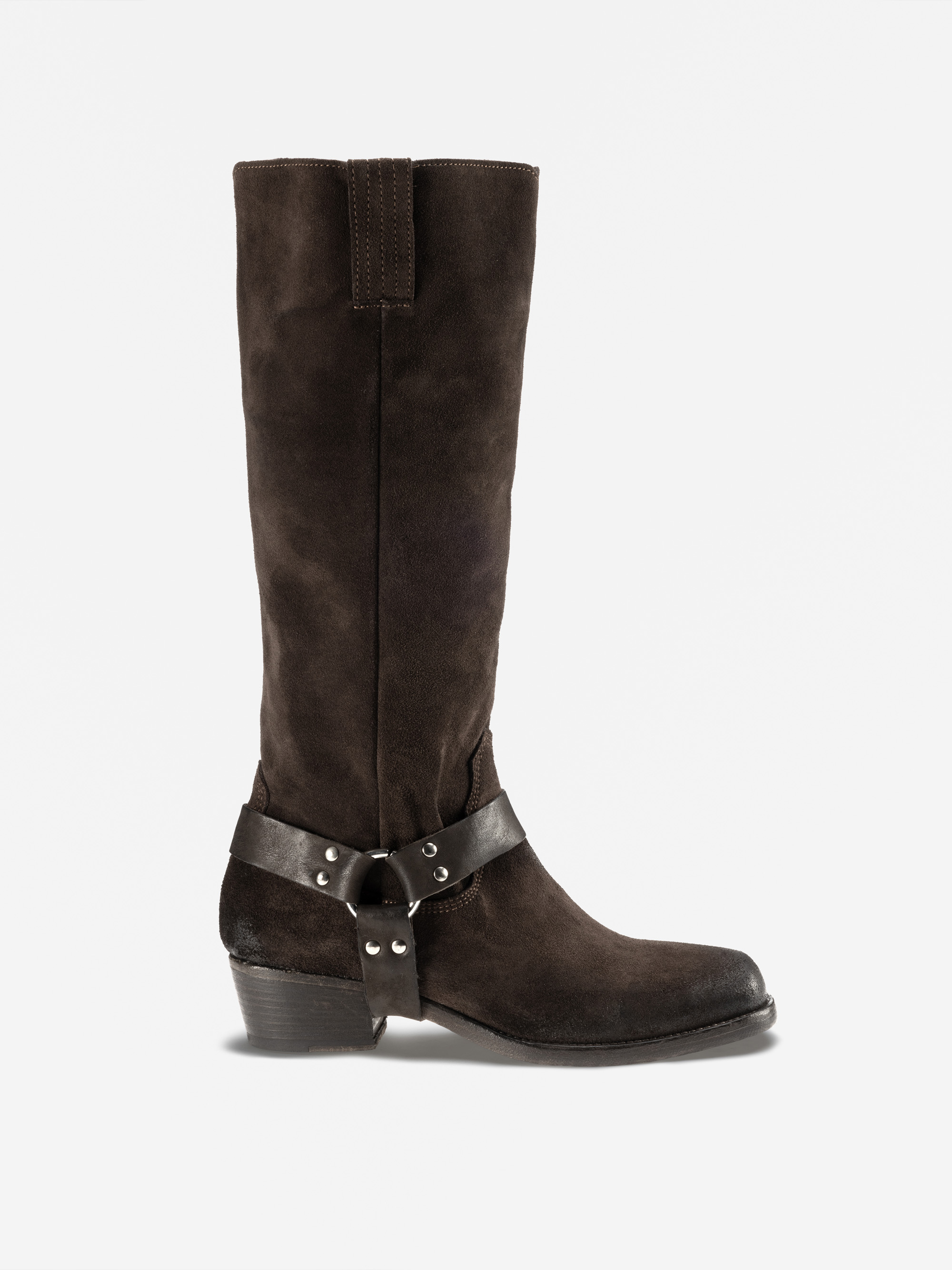 Ein hoher, dunkelbrauner Wildlederstiefel mit niedrigem Absatz, runder Spitze und einem schwarzen Ledergeschirr mit Metallnieten um den Knöchel, dargestellt auf einem schlichten weißen Hintergrund.