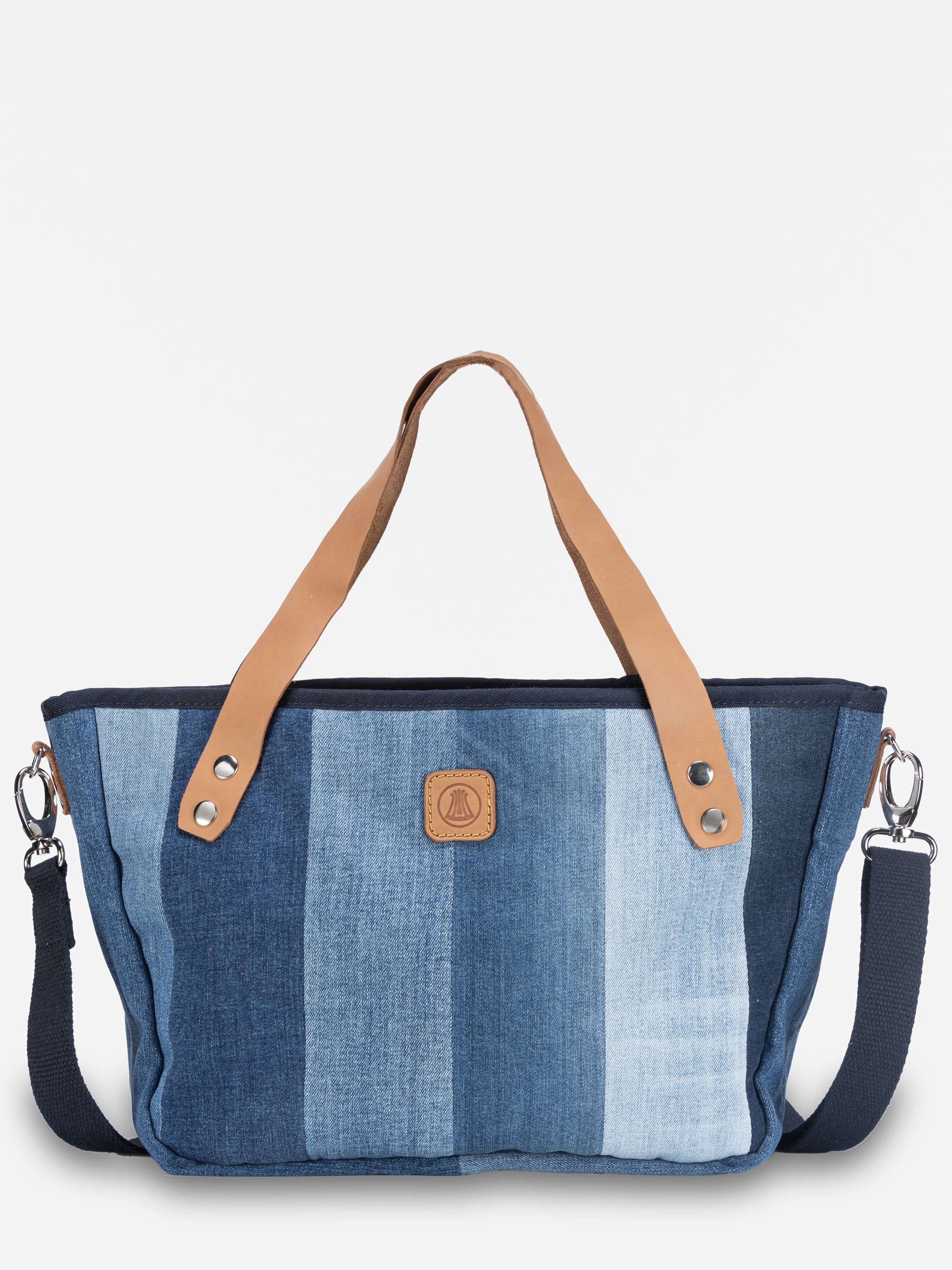 Eine Handtasche mit vertikalen jeansblauen Streifen, hellbraunen Ledergriffen, einem abnehmbaren dunkelblauen Schulterriemen und einem kleinen braunen Aufnäher in der vorderen Mitte.