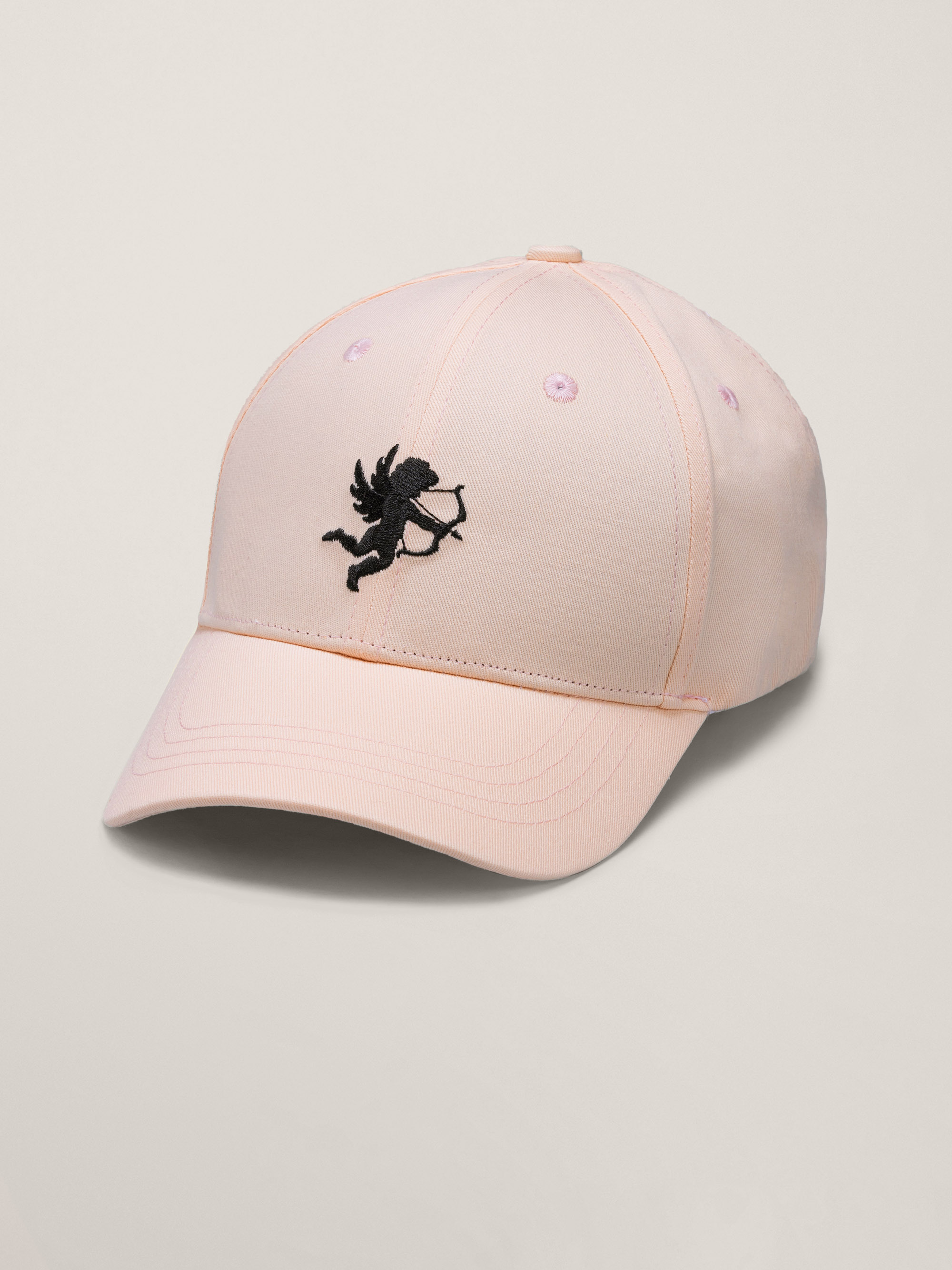 Eine hellrosa Baseballmütze mit einer schwarzen gestickten Amor-Figur mit Pfeil und Bogen auf der Vorderseite.