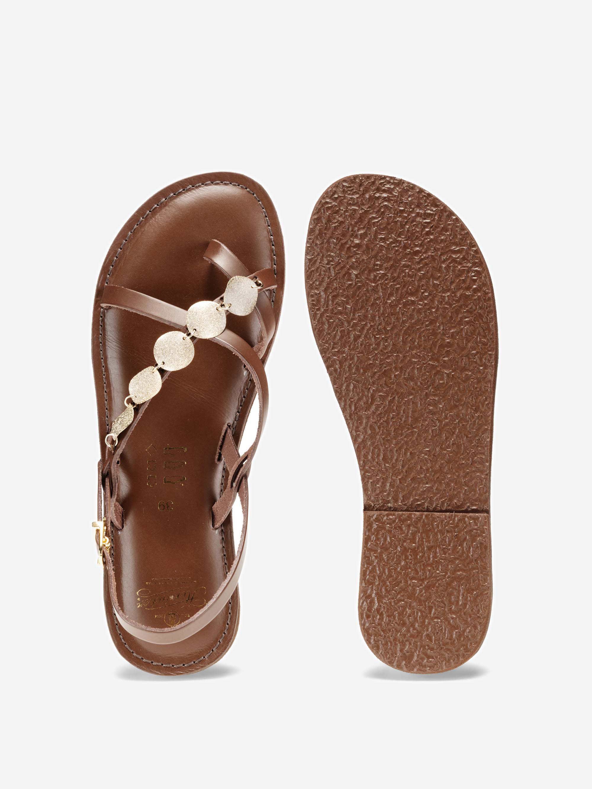 Ein Paar braune Ledersandalen; eine Sandale zeigt die Draufsicht mit goldenen kreisförmigen Verzierungen auf dem Riemen, die andere zeigt die strukturierte Sohle.