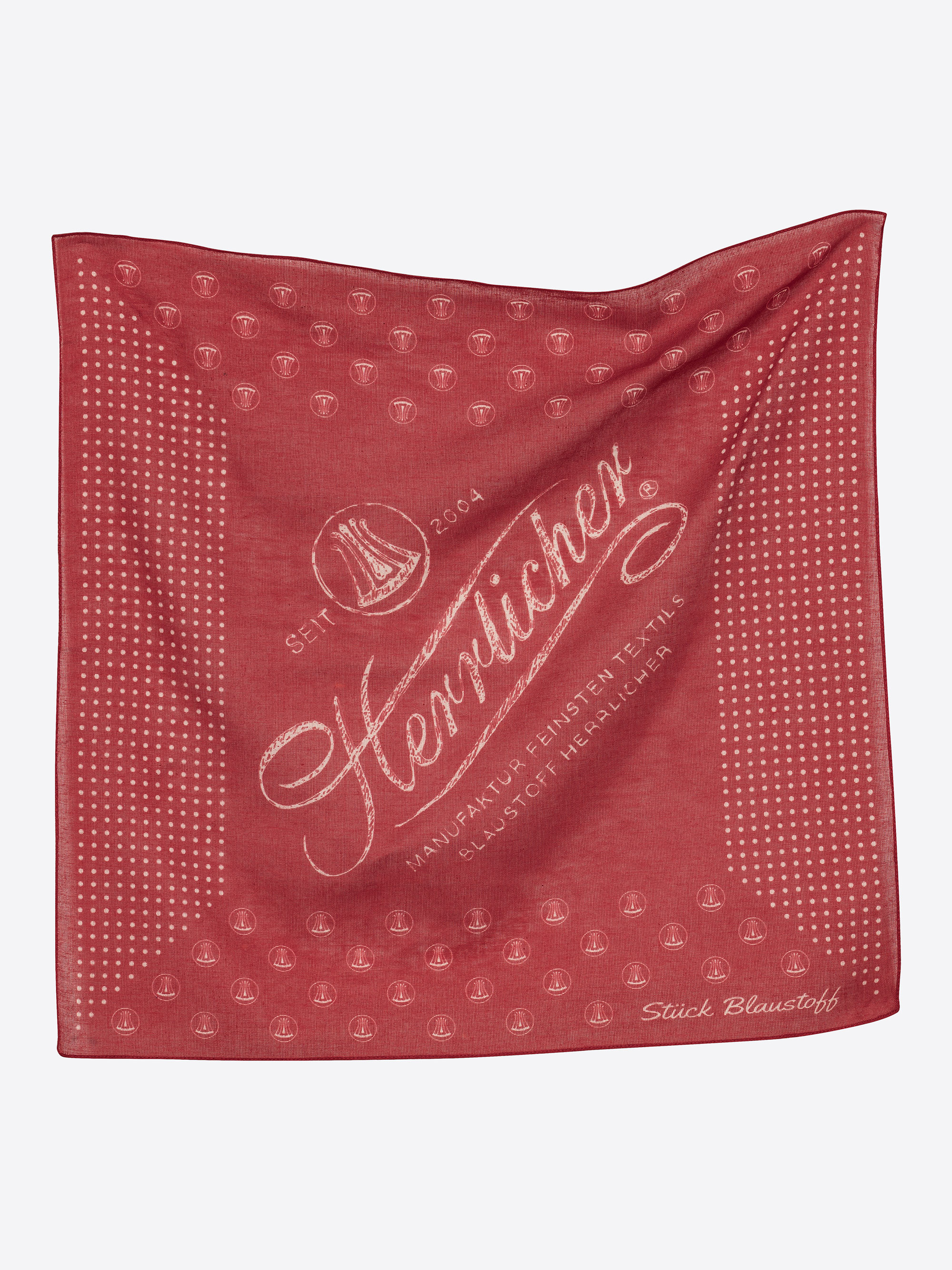 Ein rotes, quadratisches Tuch mit weißen, gepunkteten Rändern und Text, darunter Seit 1864, Hemlicher und Stück Blaustoff, zusammen mit einer Segelboot-Illustration und dekorativen Mustern.