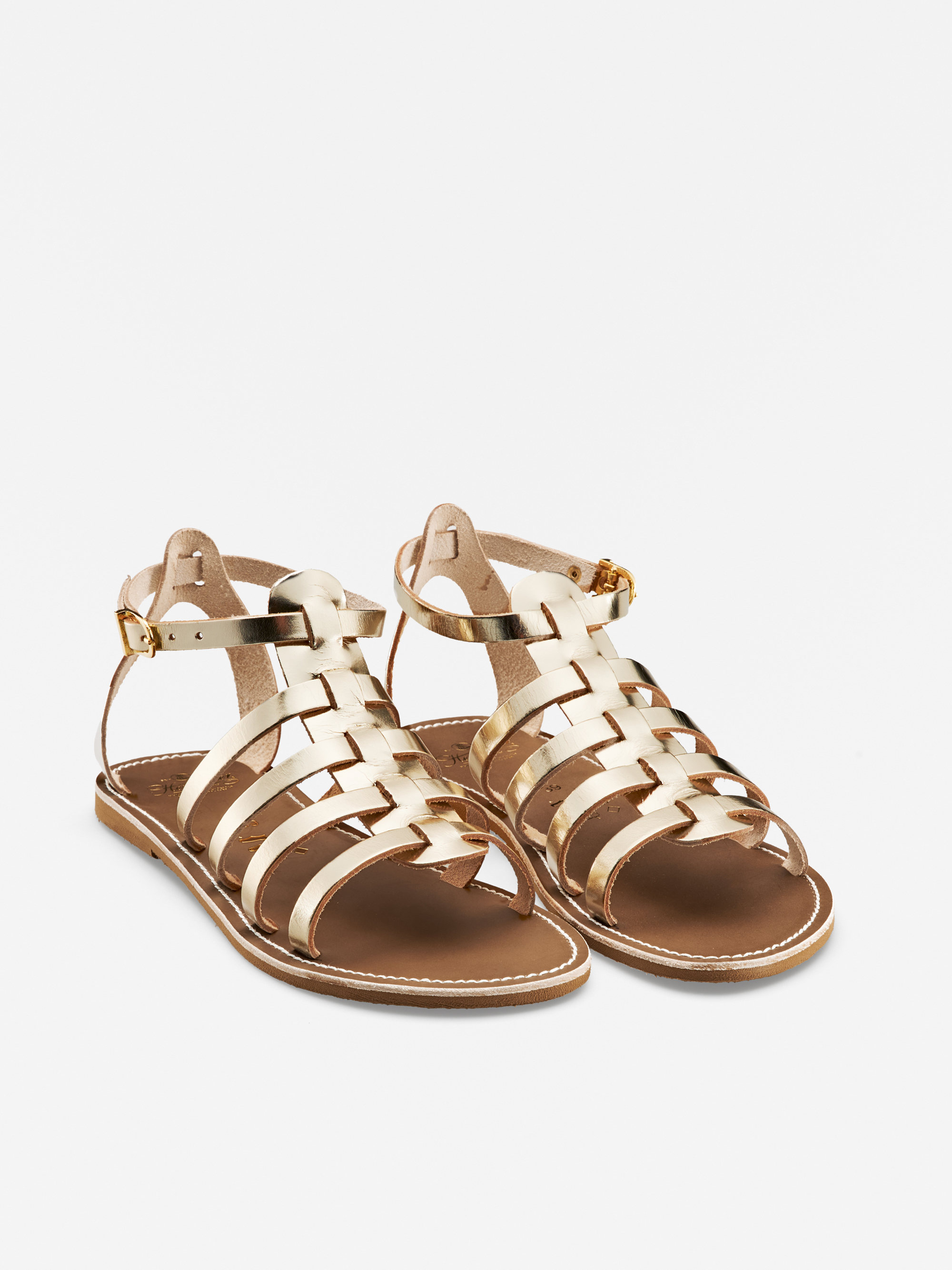 Ein Paar goldmetallisch gewebte Gladiatorensandalen mit Knöchelriemen und flachen braunen Sohlen, dargestellt auf weißem Hintergrund.