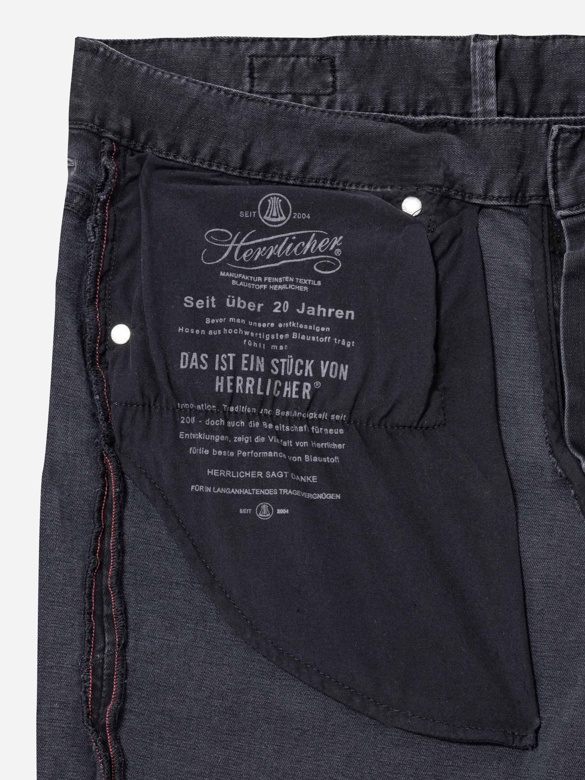 Nahaufnahme der vorderen Innentasche einer schwarzen Jeans mit weißem Branding und deutschem Text auf dem Taschenfutter sowie sichtbaren Nähten und Nieten.