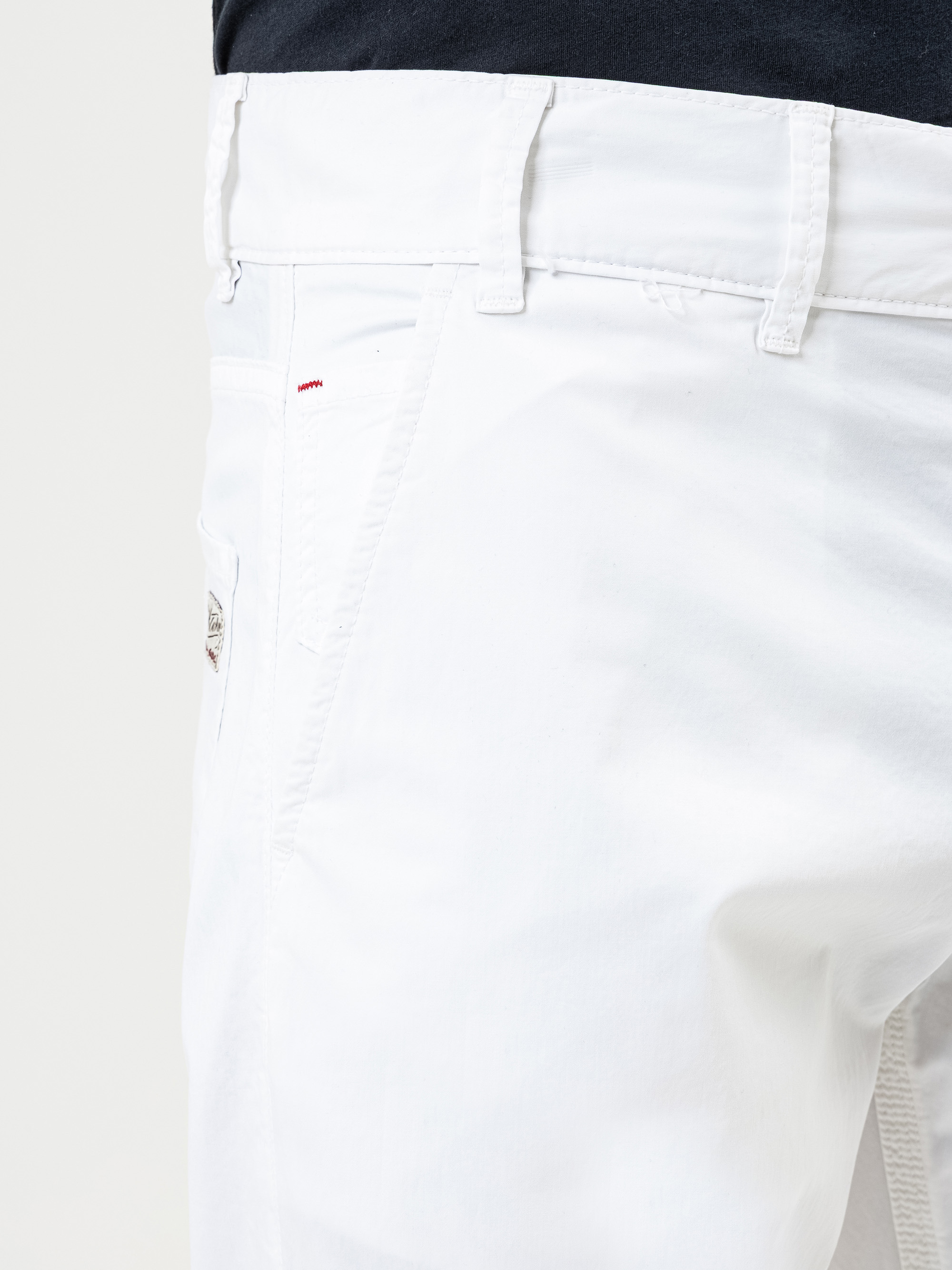 Nahaufnahme einer Person, die eine weiße Hose mit Gürtelschlaufen und einer sichtbaren Seitentasche trägt, gepaart mit einem dunklen Oberteil. Das Bild konzentriert sich auf den Hüft- und Oberschenkelbereich.