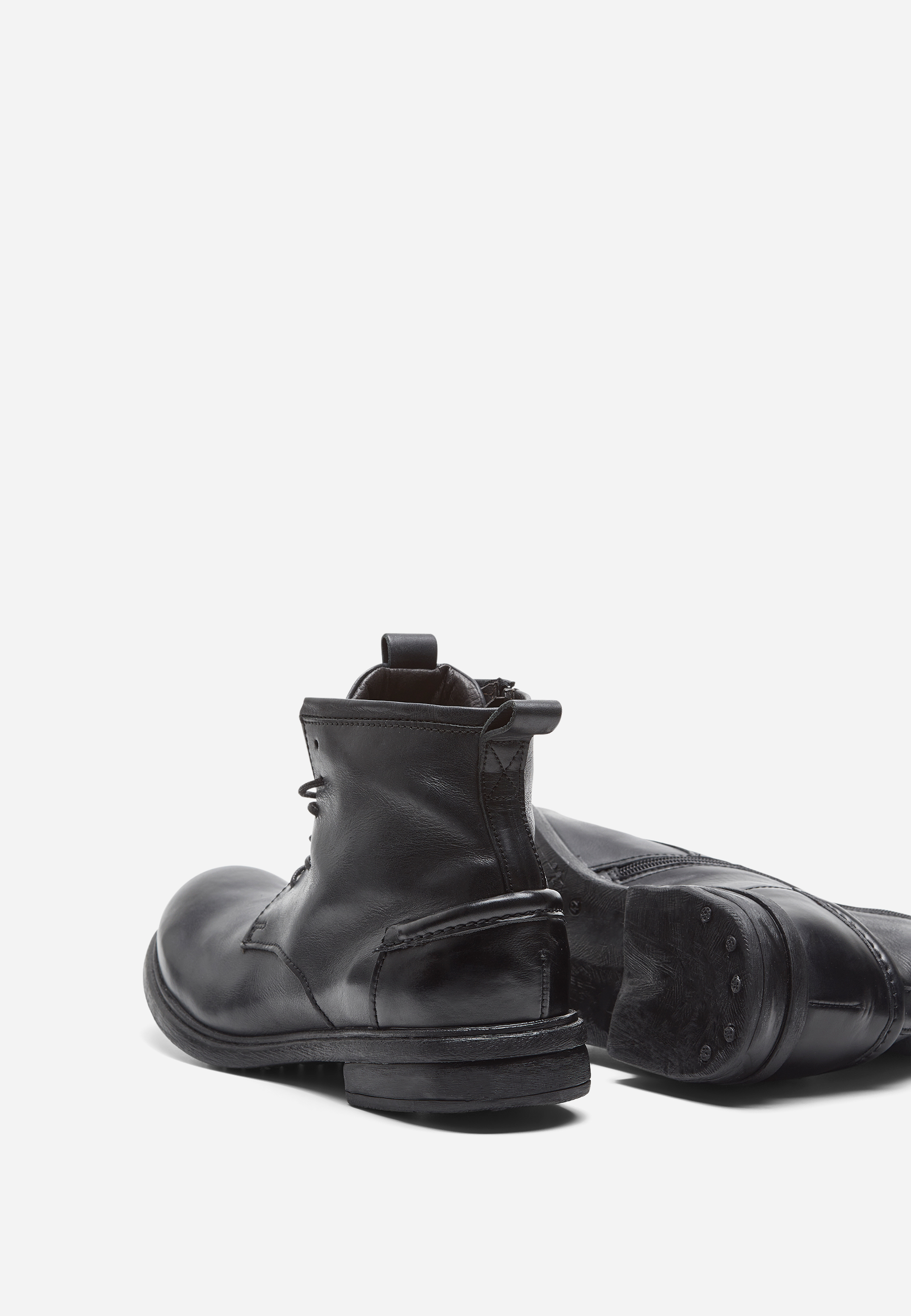 Ein Paar schwarze Lederstiefel, einer aufrecht und einer auf der Seite liegend, mit strukturierter Sohle und Reißverschluss auf der Rückseite, vor einem schlichten weißen Hintergrund.