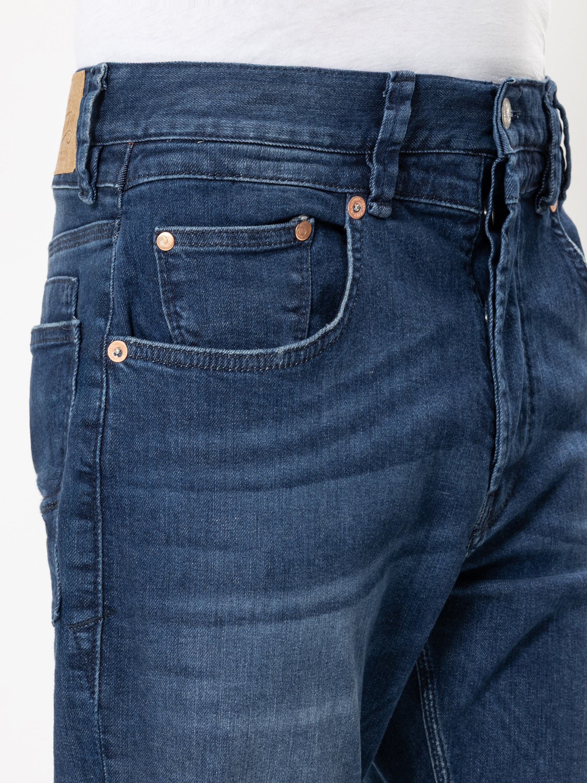 Nahaufnahme einer Person, die eine blaue Jeans und ein weißes Hemd trägt, wobei der Schwerpunkt auf der vorderen Tasche und dem Bund der Jeans liegt.