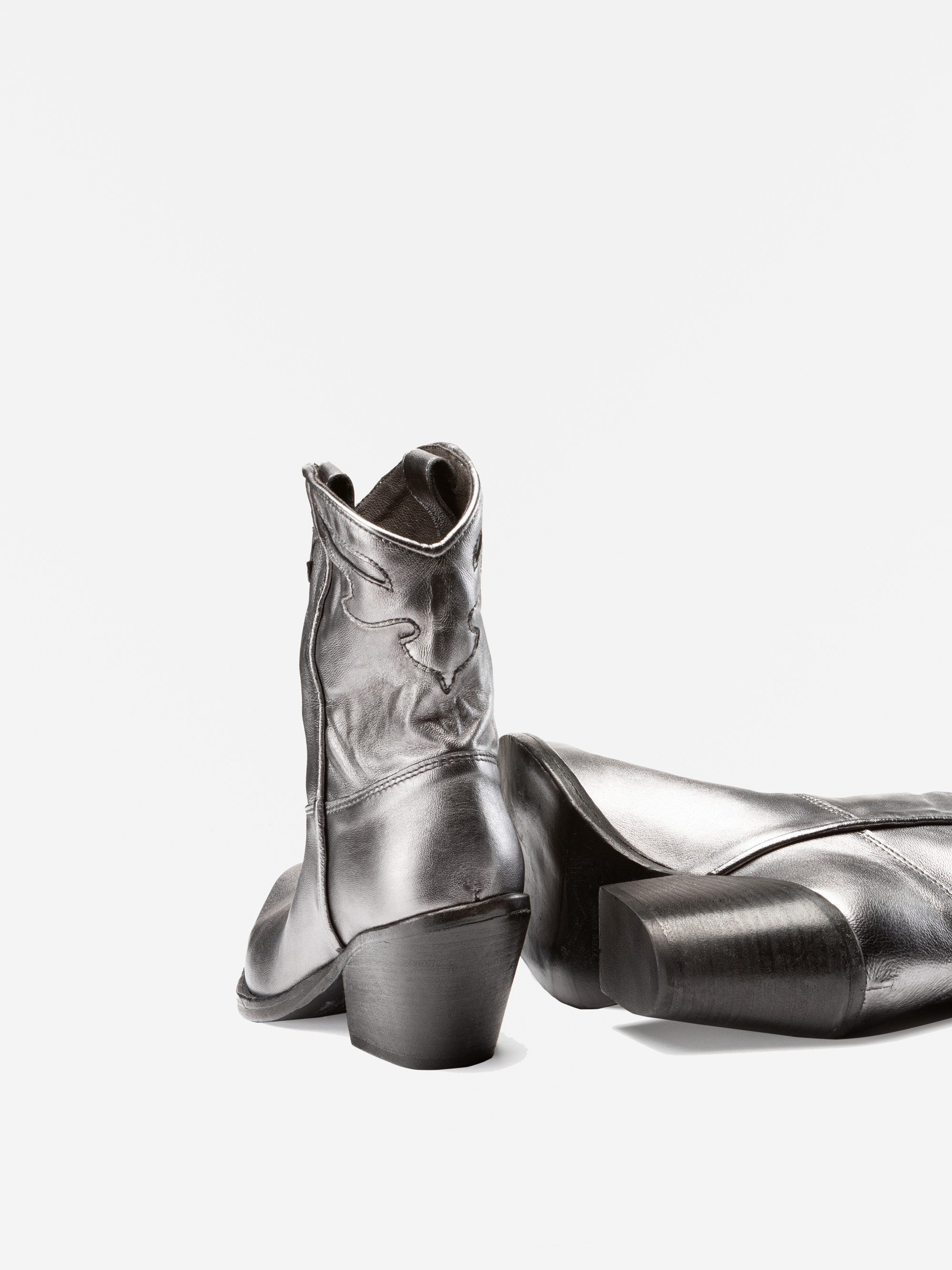 Ein Paar silbern glänzender, halbhoher Cowboystiefel mit gestapelten Absätzen, wobei ein Stiefel aufrecht steht und der andere auf der Seite liegt, dargestellt auf einem weißen Hintergrund.