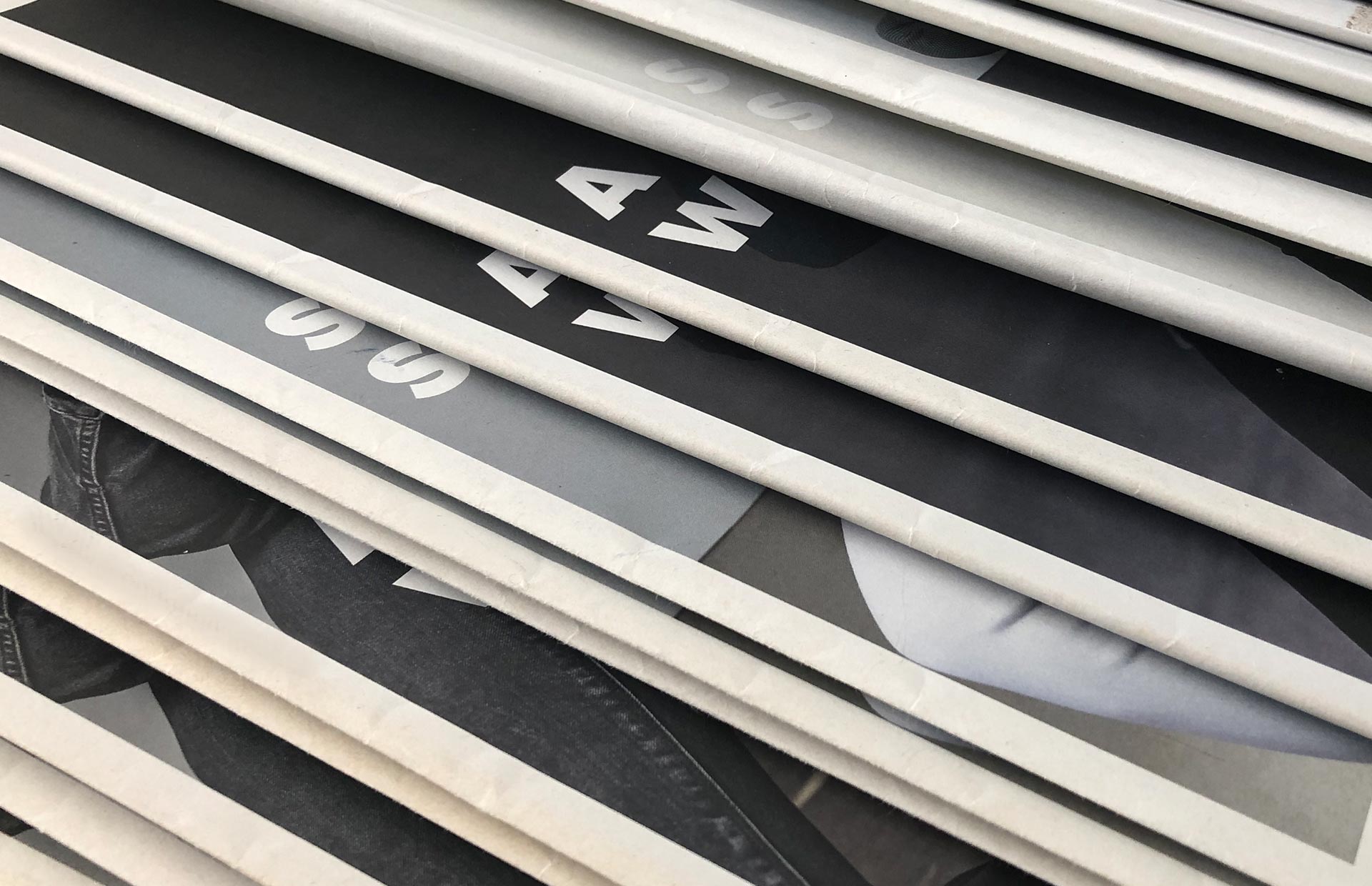 Mehrere gestapelte Zeitungen oder Zeitschriften sind teilweise mit weißen horizontalen Latten abgedeckt, die die gedruckten Buchstaben und Schwarz-Weiß-Bilder darunter verdecken.