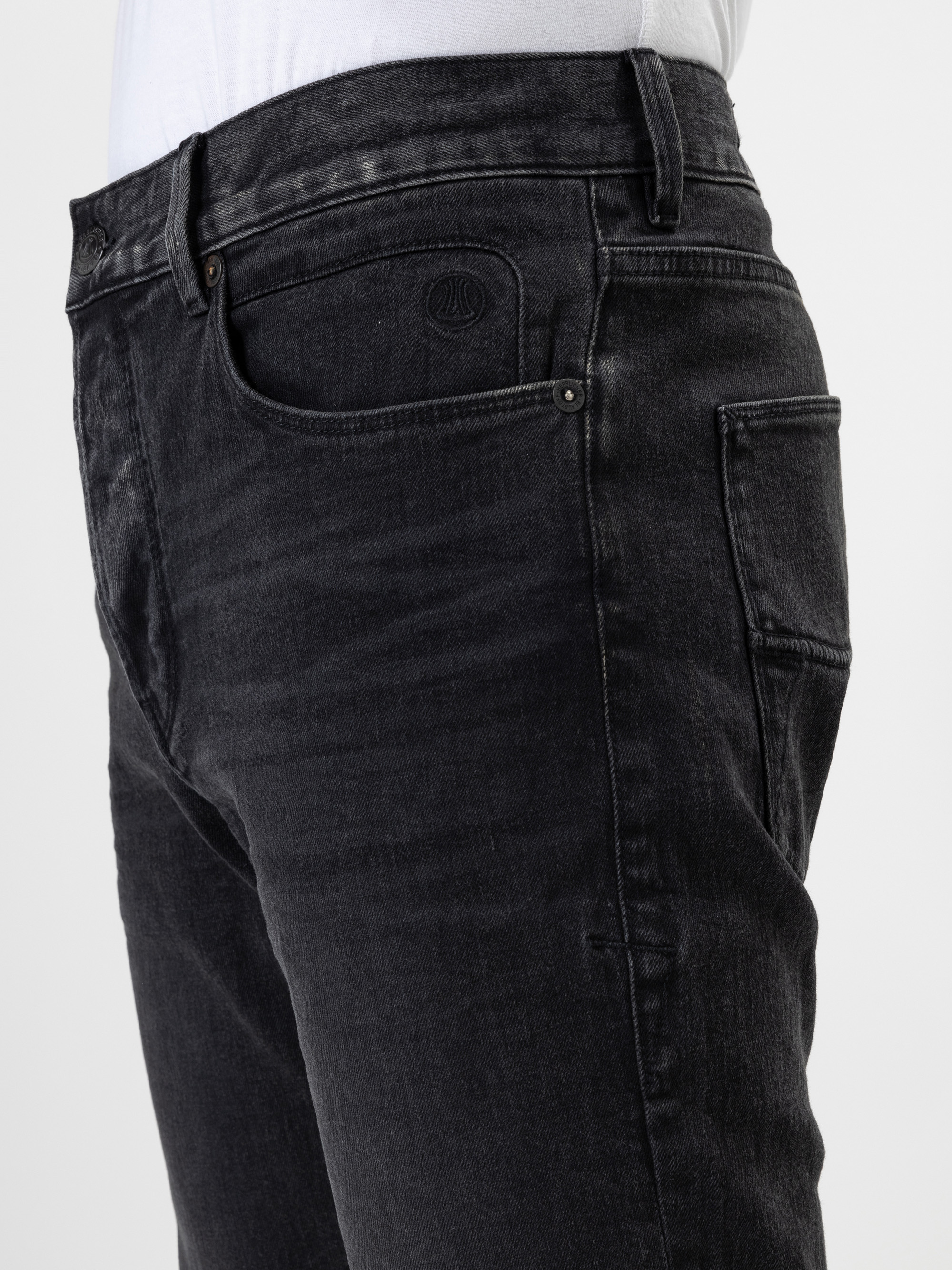 Seitliche Nahaufnahme einer Person, die eine schwarze Jeans und ein weißes Hemd trägt, wobei der Schwerpunkt auf der Taille, der Tasche und dem Oberschenkelbereich liegt.