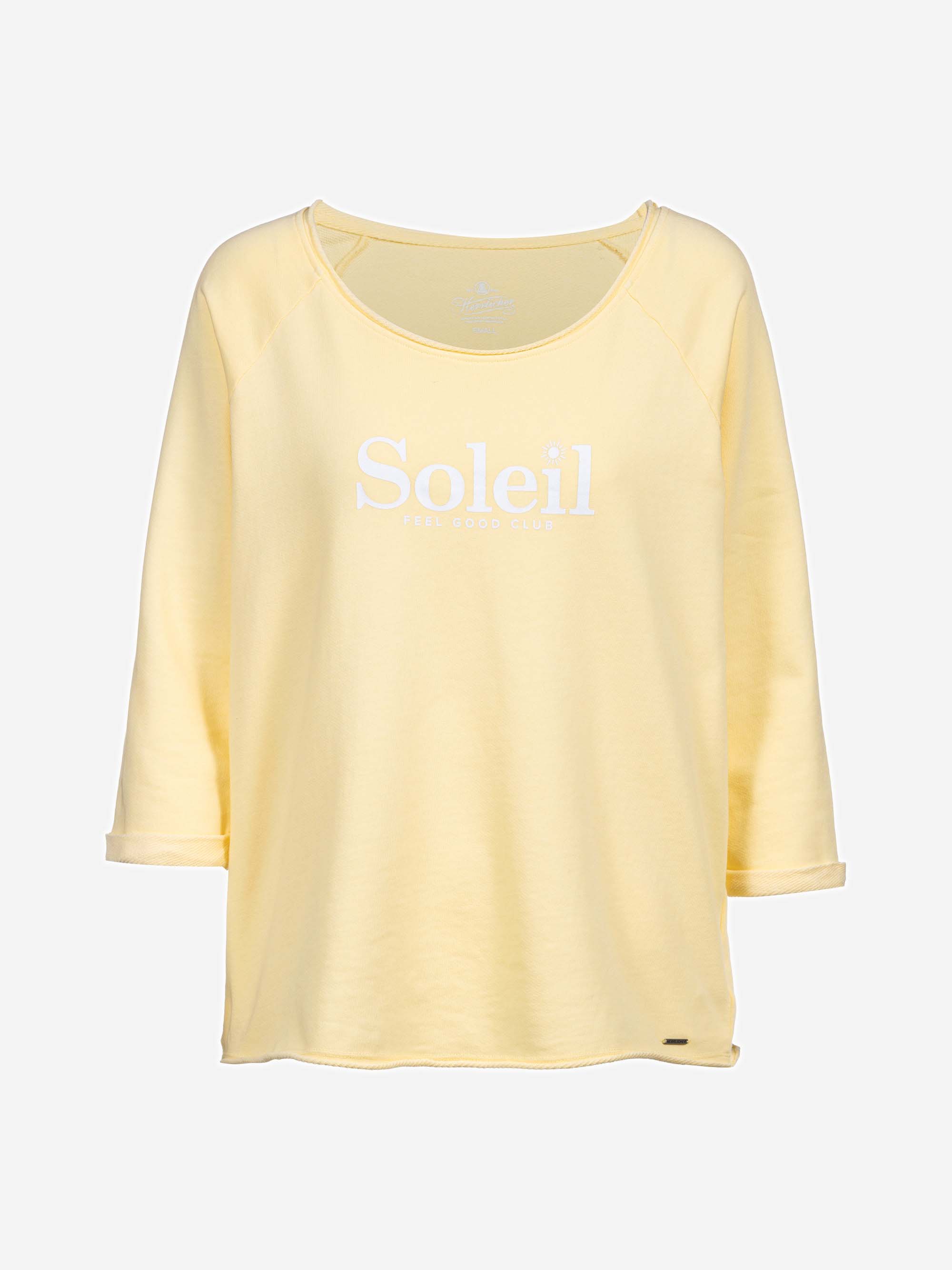 Ein hellgelbes, dreiviertelärmeliges Shirt mit rundem Ausschnitt. Auf der Vorderseite steht in großen weißen Buchstaben das Wort Soleil, darunter der kleinere Text FEEL GOOD CLUB.