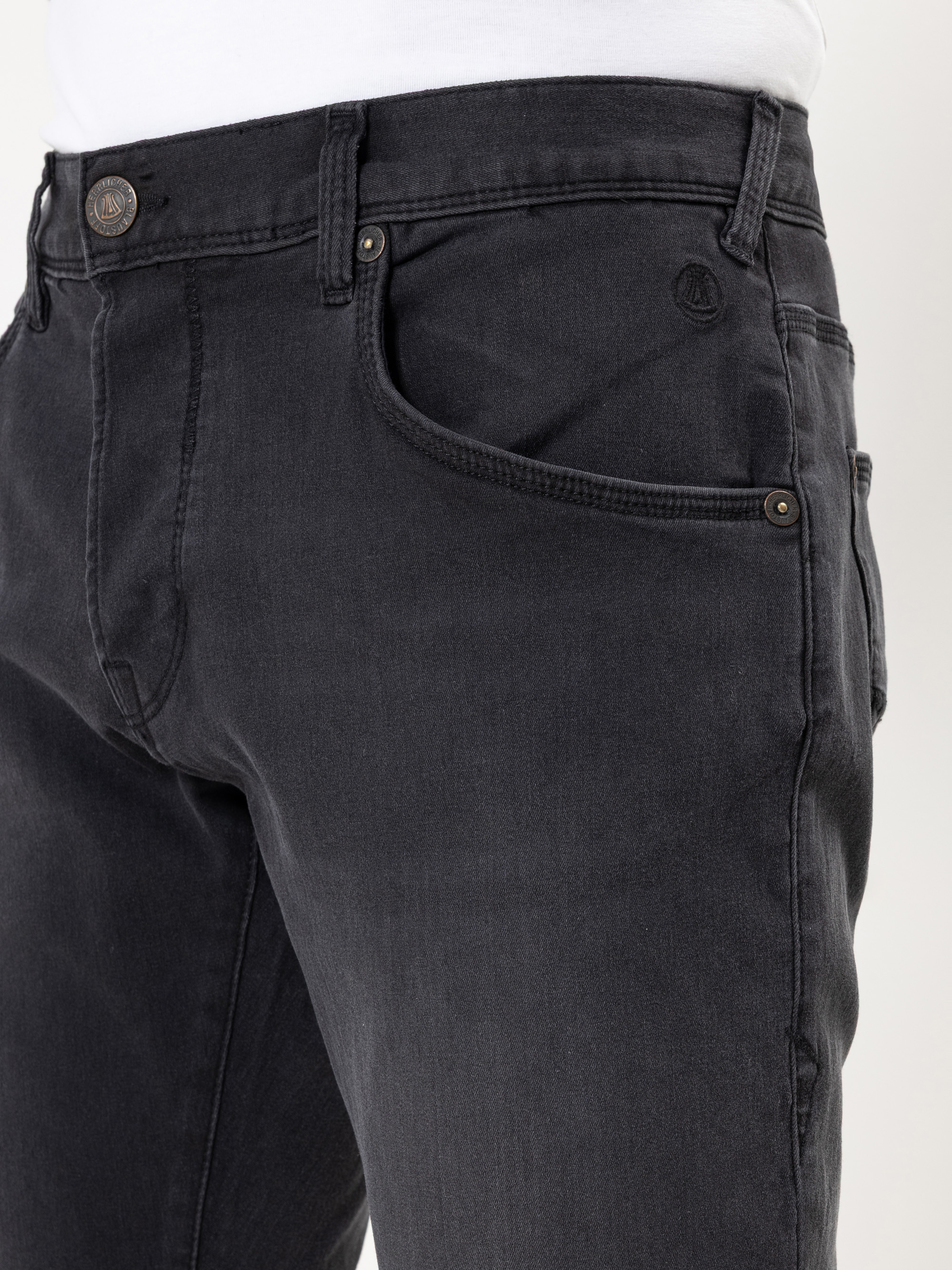 Nahaufnahme einer Person, die eine schwarze Jeans und ein weißes Hemd trägt, wobei die Vordertaschen, der Hosenbund und die Knöpfe zu sehen sind.