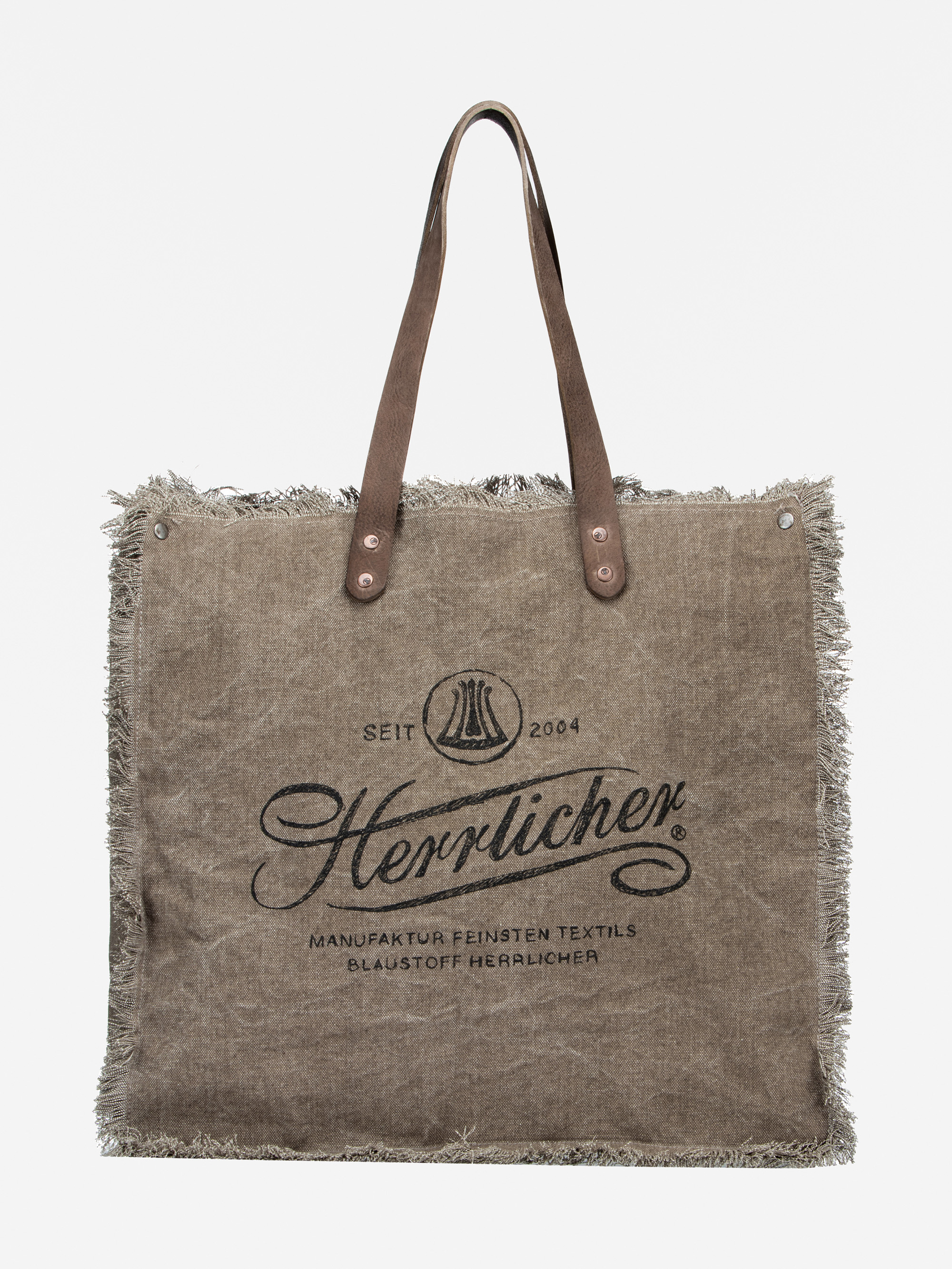 Eine braune, rechteckige Tragetasche aus Stoff mit ausgefransten Rändern, zwei Ledergriffen und schwarzem Text und Logo auf der Vorderseite mit der Aufschrift Herrlicher und anderen deutschen Ausdrücken. Der Hintergrund ist einfarbig weiß.