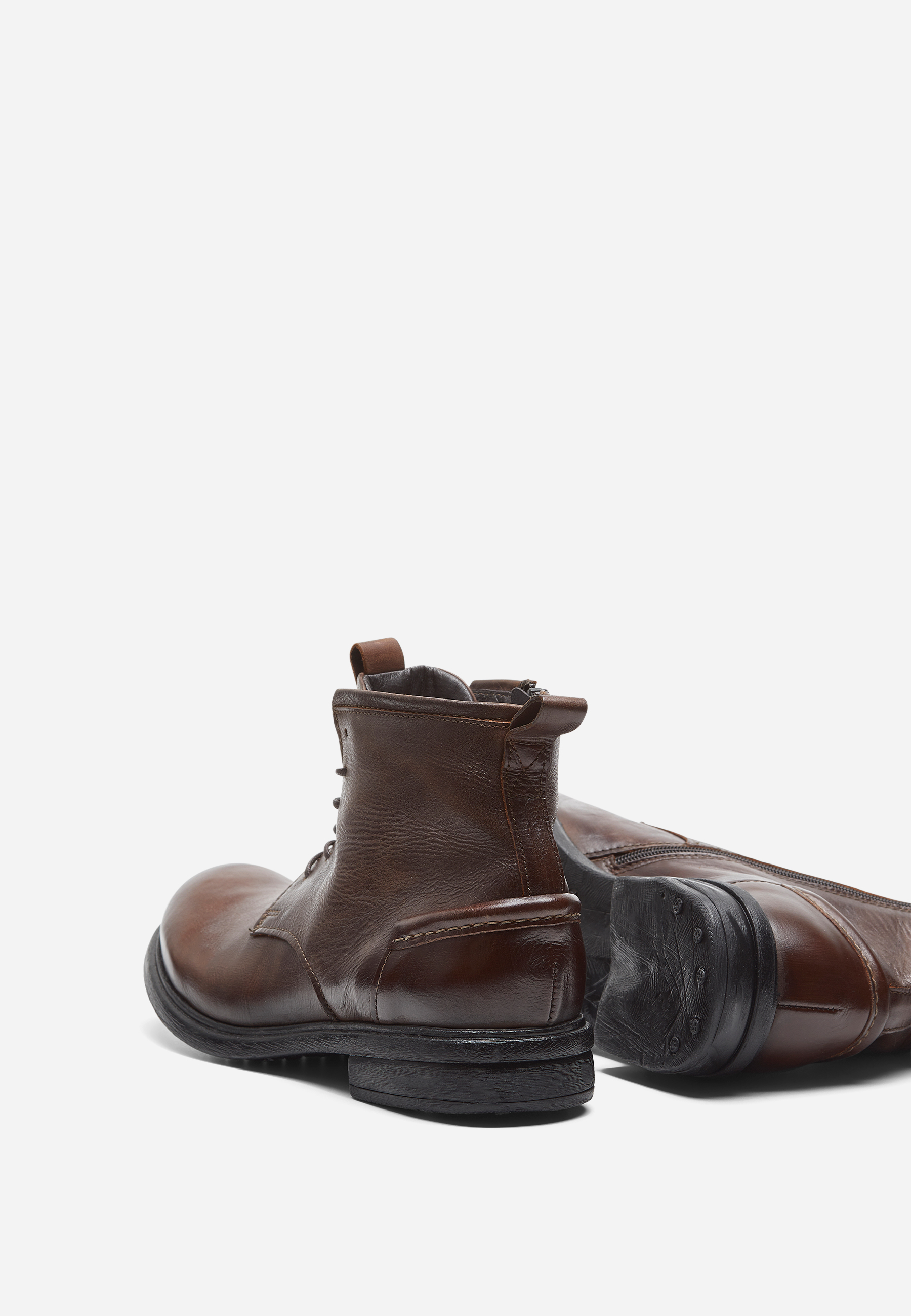 Ein Paar braune Lederschnürstiefel mit schwarzen Sohlen. Ein Stiefel steht aufrecht, mit dem Gesicht nach außen, während der andere auf der Seite liegt, so dass die Sohle sichtbar ist. Der Hintergrund ist einfarbig weiß.