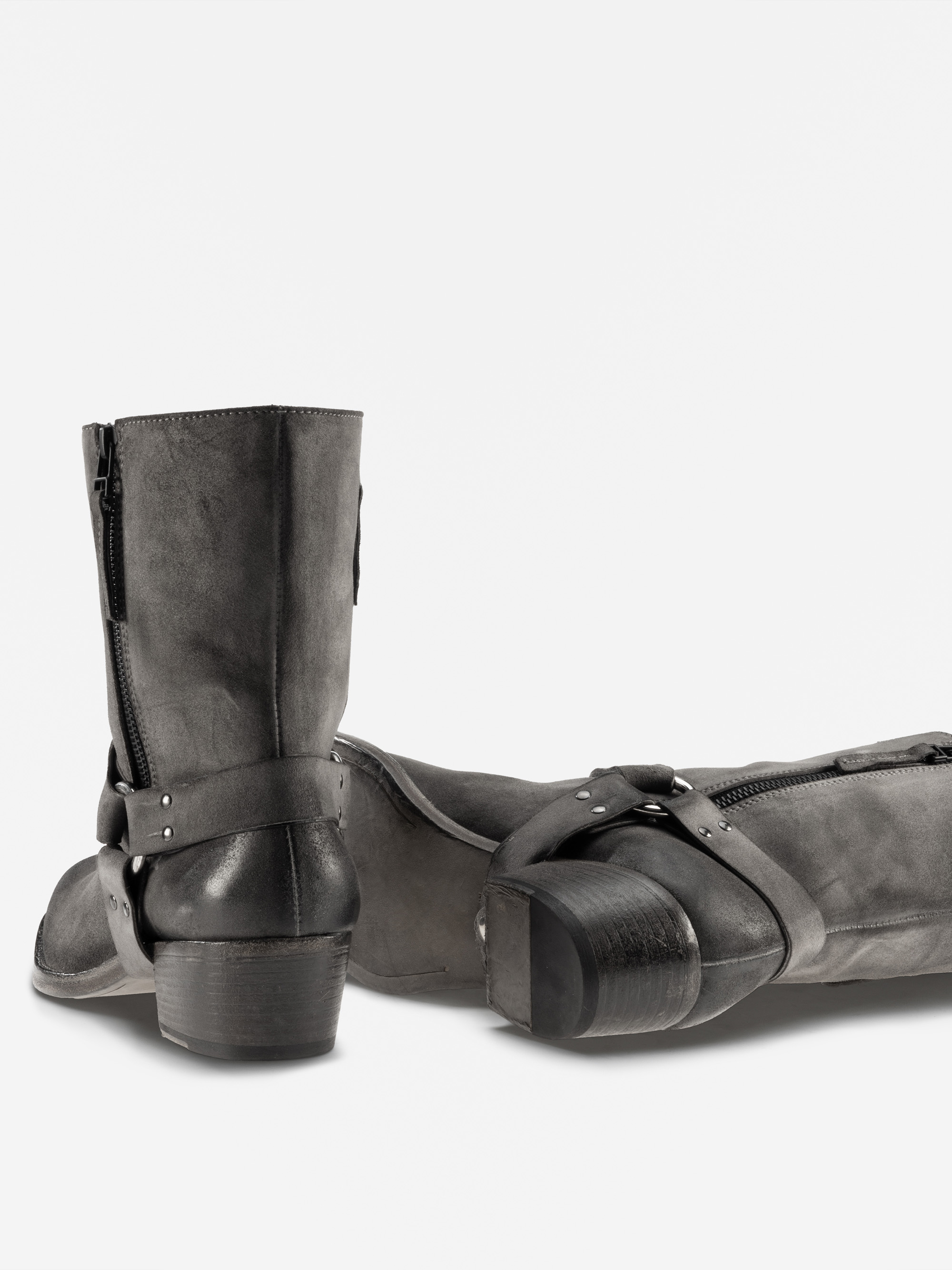 Ein Paar schwarzer Lederknöchelstiefel mit seitlichen Reißverschlüssen und Trageriemen, wobei ein Stiefel aufrecht steht und der andere auf der Seite liegt, dargestellt vor einem schlichten weißen Hintergrund.