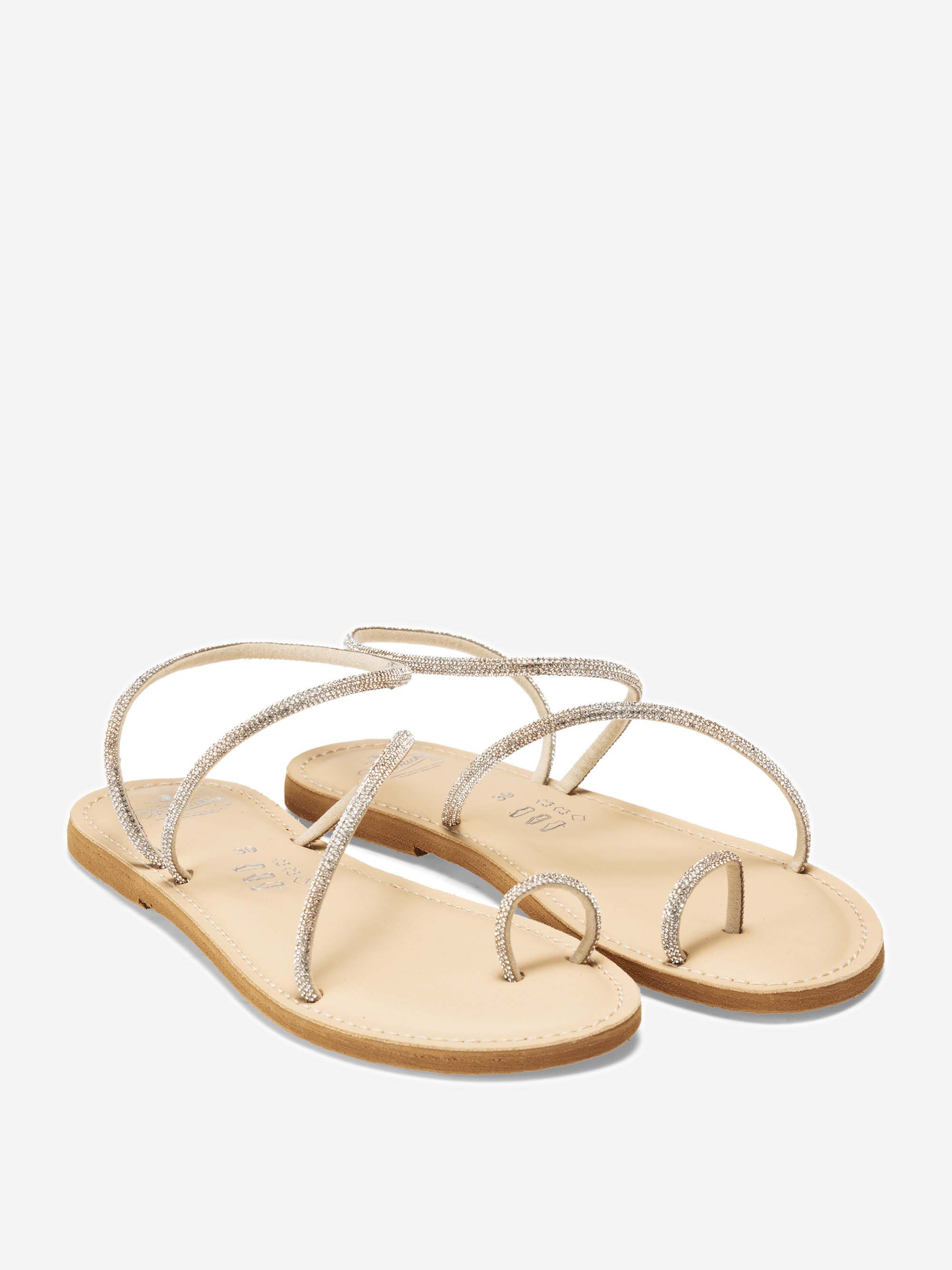 Beigefarbene flache Sandalen mit dünnen, glitzernden, sich kreuzenden Riemen und einer Zehenschlaufe auf weißem Hintergrund.