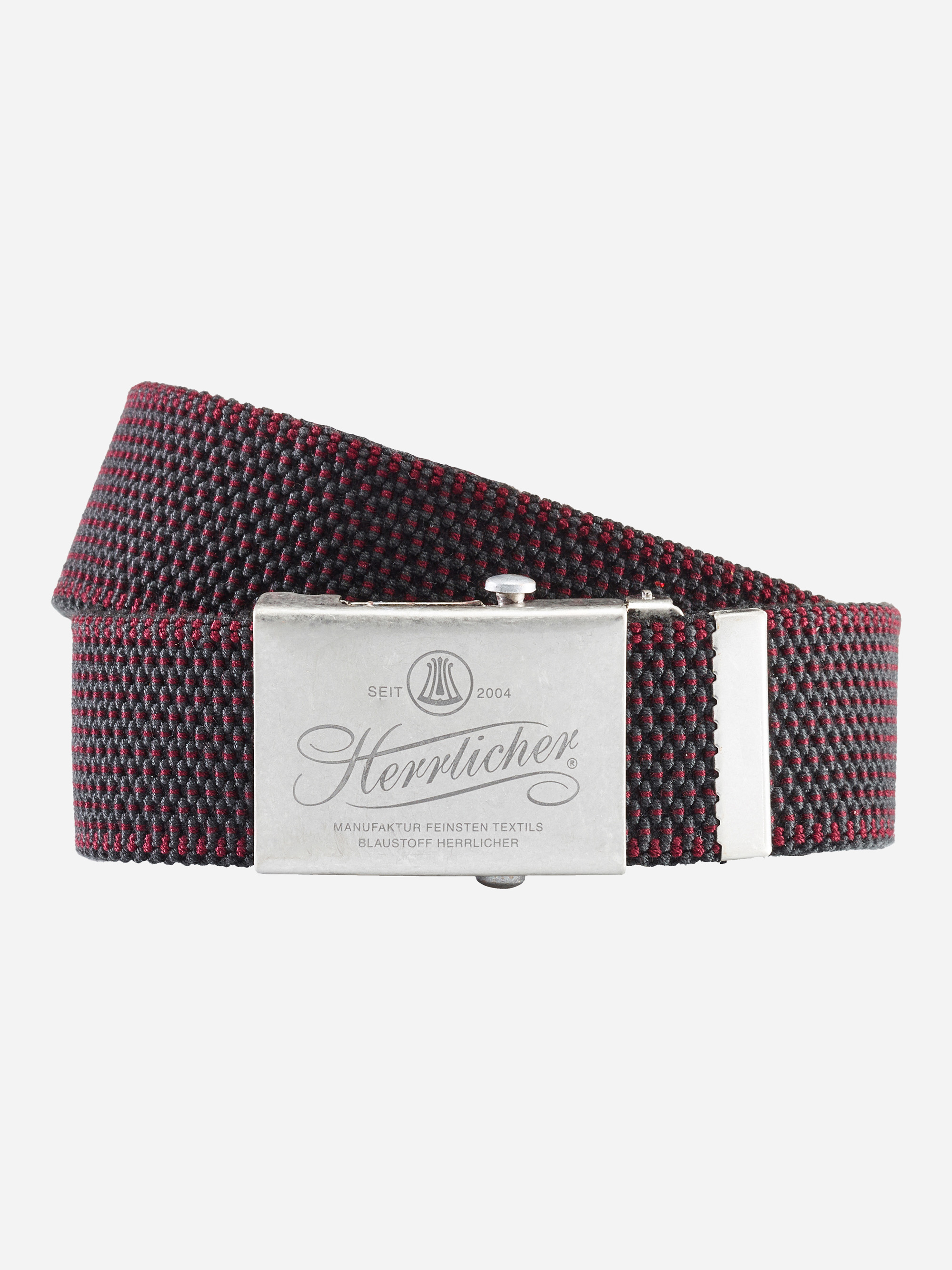 Ein gewebter, dunkelroter und schwarzer Stoffgürtel mit einer silbernen, rechteckigen Metallschnalle, auf der Herrlicher und zusätzlicher Text eingraviert sind, aufgerollt auf einem schlichten, hellen Hintergrund.