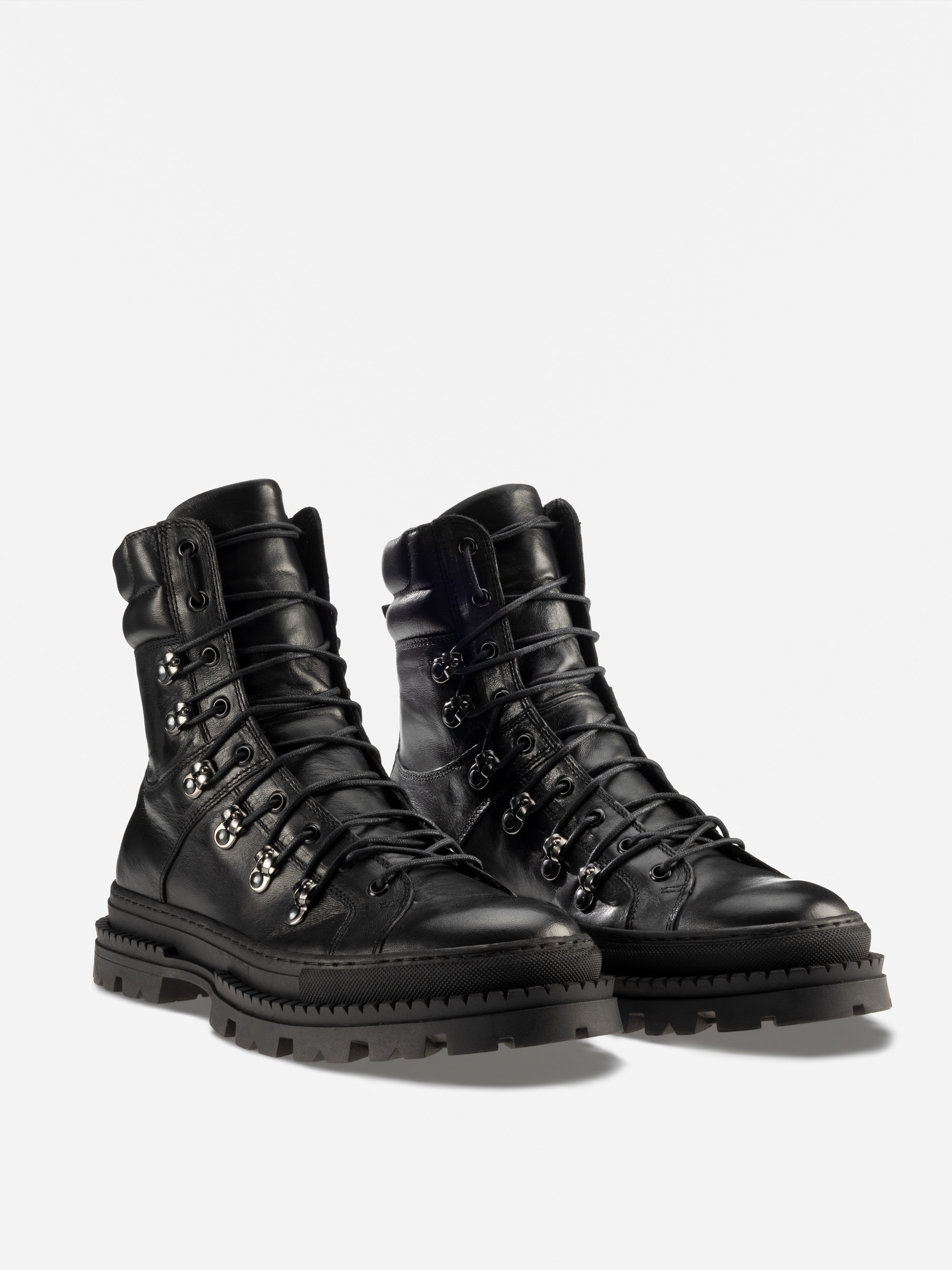 Ein Paar schwarze Lederschnürstiefel mit klobigen Stollensohlen und Metallösen auf weißem Hintergrund.