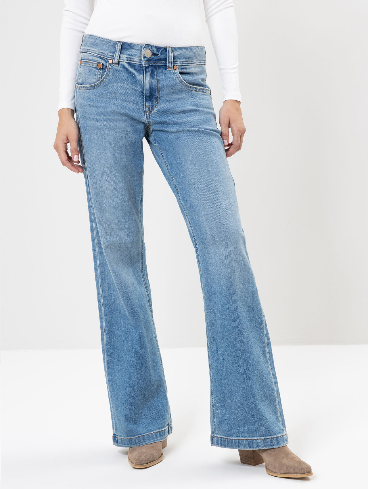 Eine Person, die hellblaue Jeans mit hoher Taille und weitem Bein, ein weißes langärmeliges Oberteil und beigefarbene Schuhe mit Absatz trägt, steht vor einem schlichten hellen Hintergrund.