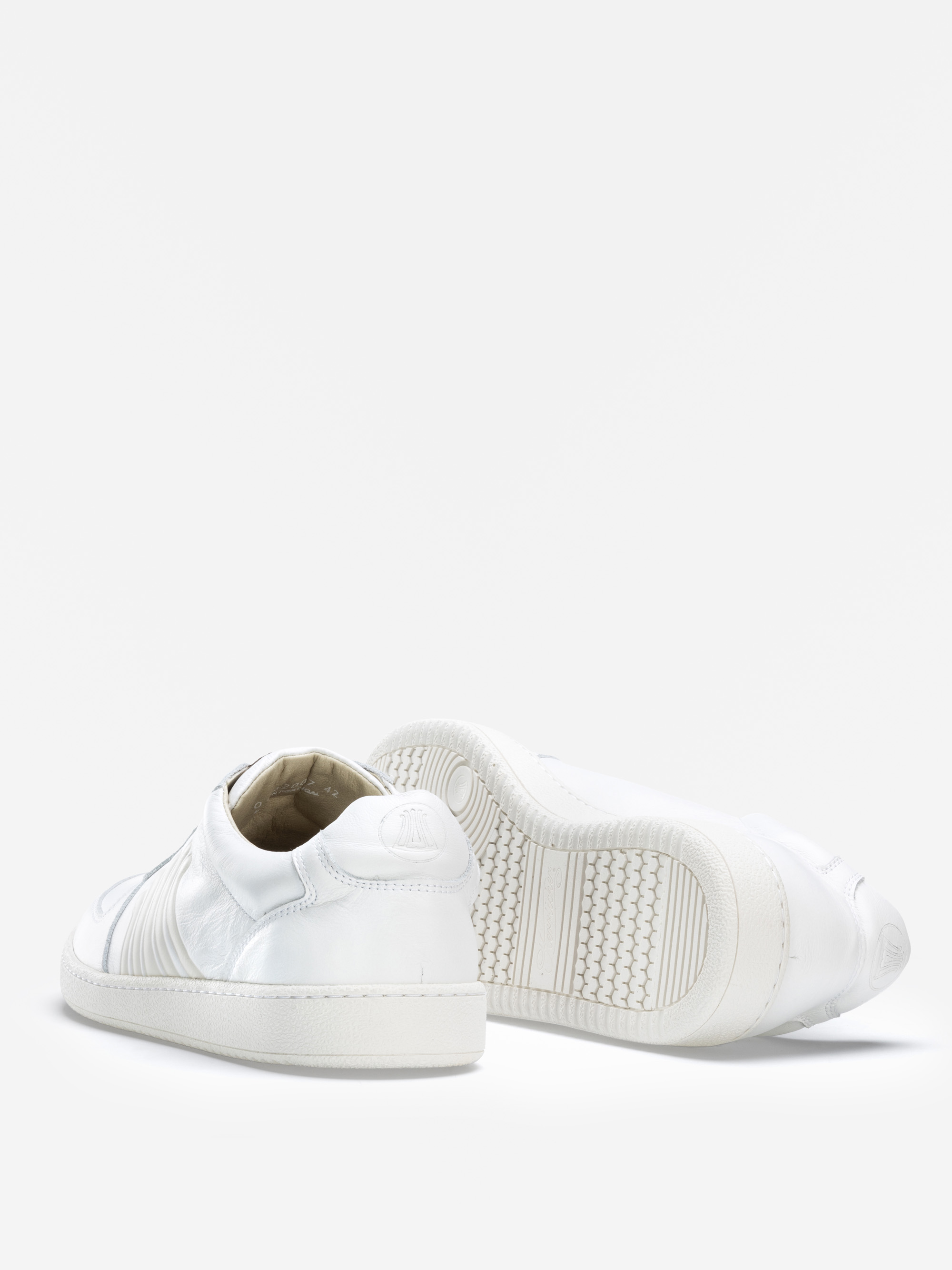 Abgebildet ist ein Paar weißer Low-Top-Sneaker, wobei ein Schuh aufrecht steht und der andere auf der Seite liegt, um die strukturierte Sohle und die Nähte auf einem einfarbig weißen Hintergrund zu zeigen.