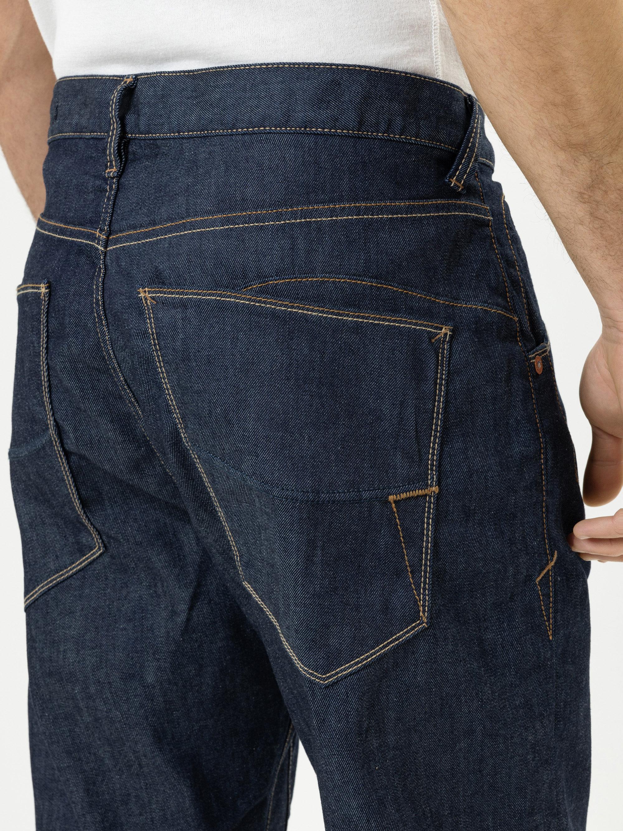 Nahaufnahme einer Person, die eine dunkelblaue Jeans trägt, wobei die Gesäßtaschen mit markanten orangefarbenen Nähten zu sehen sind. Die Person trägt außerdem ein weißes Hemd, das in die Jeans gesteckt wird.