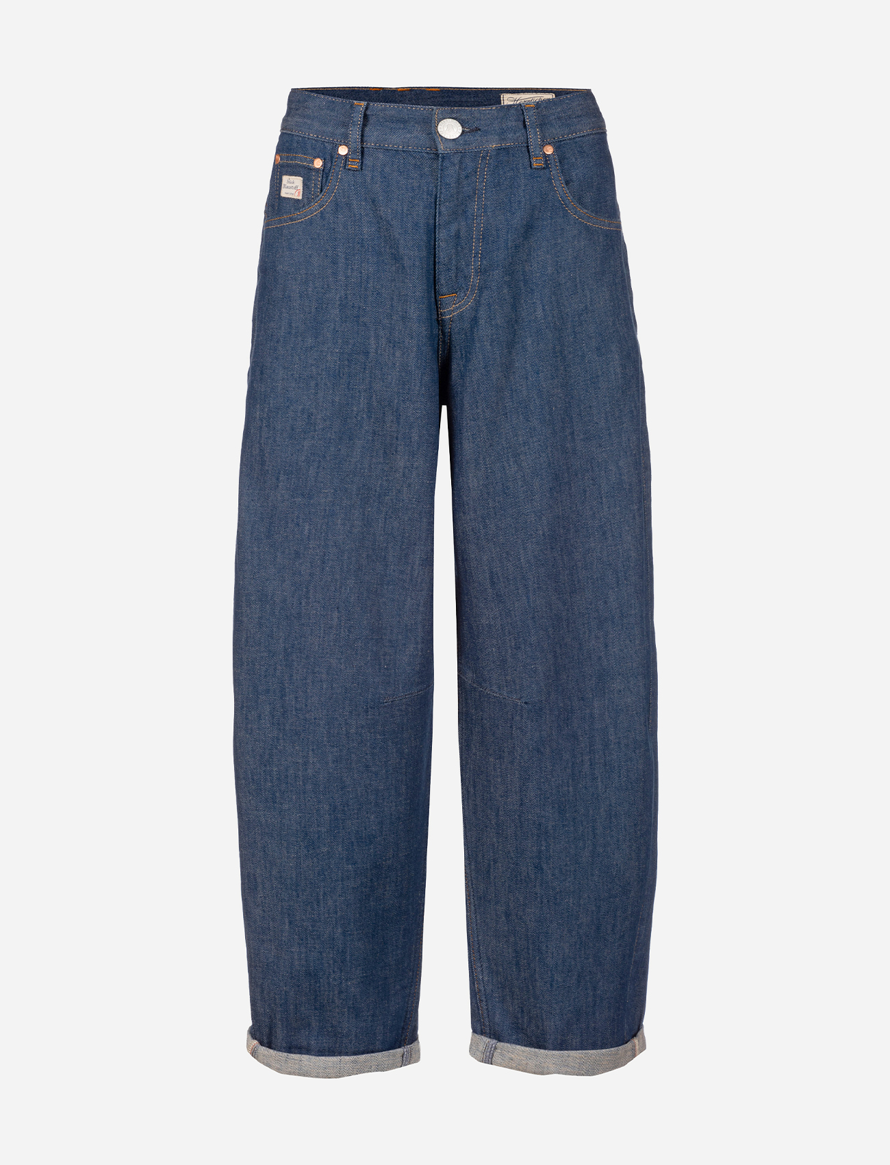 Eine Frau steht vor einem schlichten Hintergrund und trägt ein ärmelloses Jeanshemd über einem weißen Oberteil, hellblaue Jeans mit weitem Bein und weiße Turnschuhe. Sie hat langes blondes Haar und einen neutralen Gesichtsausdruck.