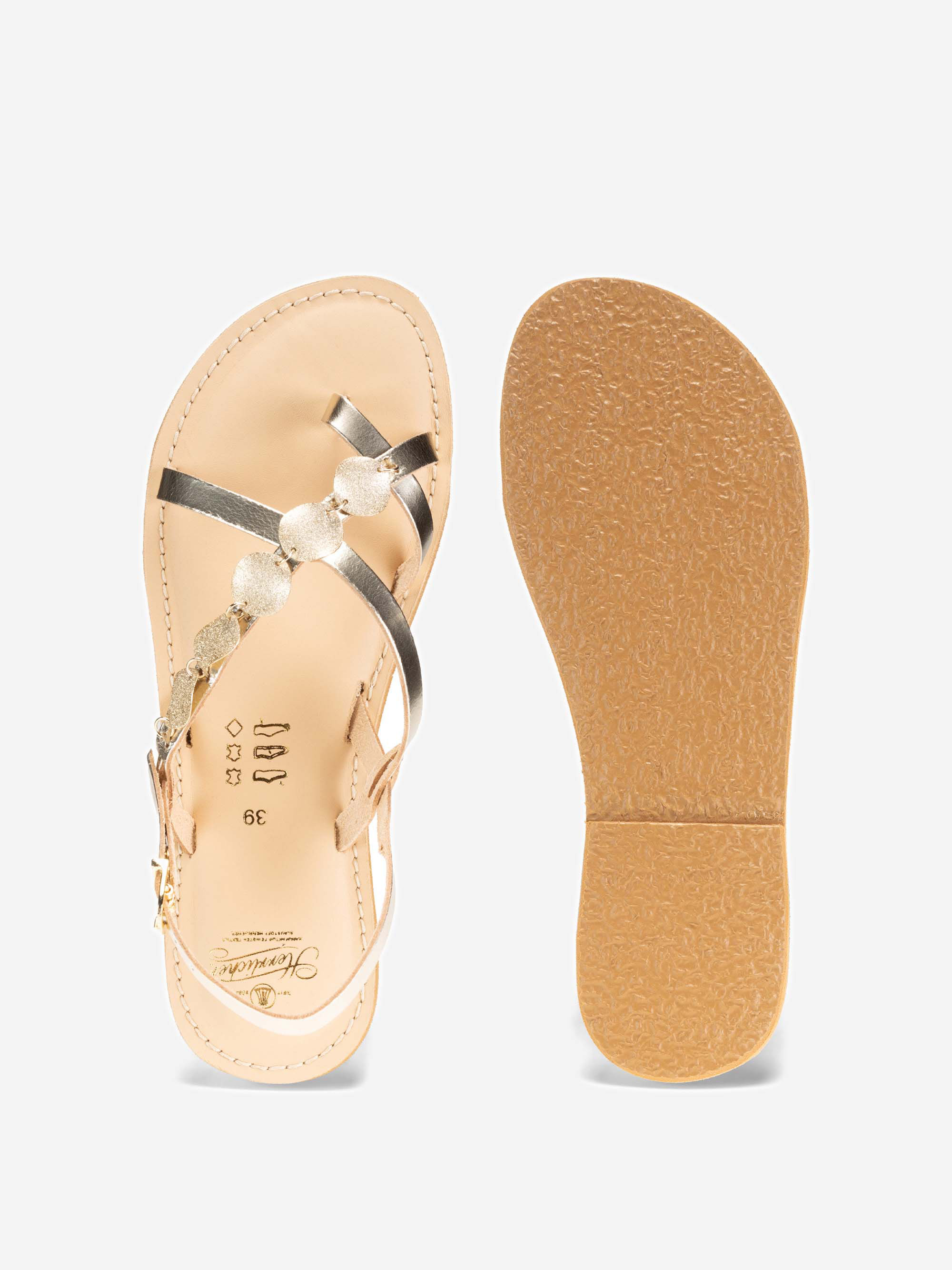 Ein Paar beigefarbene flache Sandalen mit metallischen Riemen und dekorativen Perlen, gezeigt von oben und von unten, um die Sohle und das obere Design auf weißem Hintergrund zu zeigen.