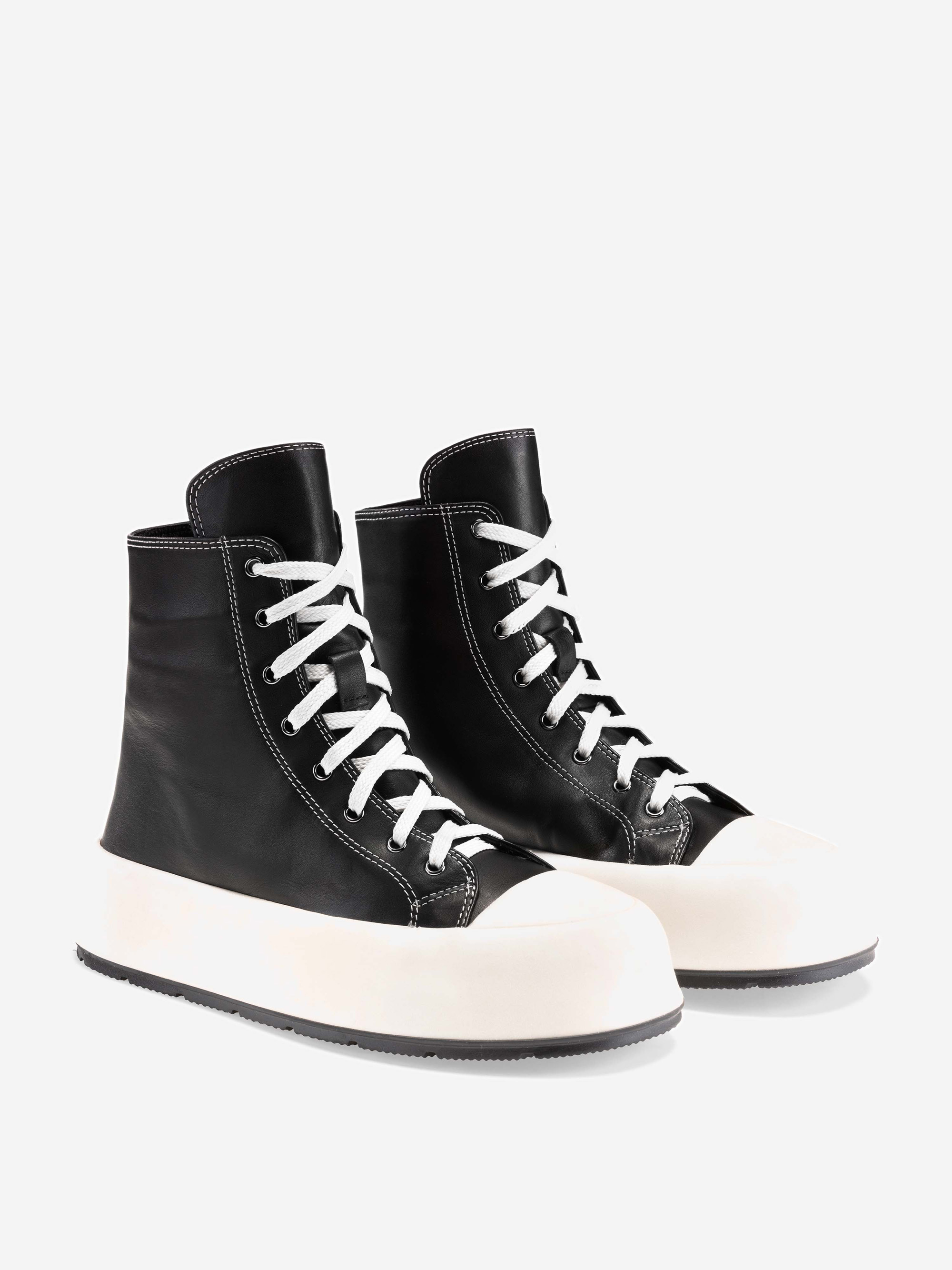 Ein Paar High-Top-Sneakers mit schwarzem Obermaterial aus Leder, weißen Schnürsenkeln, weißen Zehenkappen aus Gummi und dicken weißen Sohlen, dargestellt auf einem schlichten weißen Hintergrund.