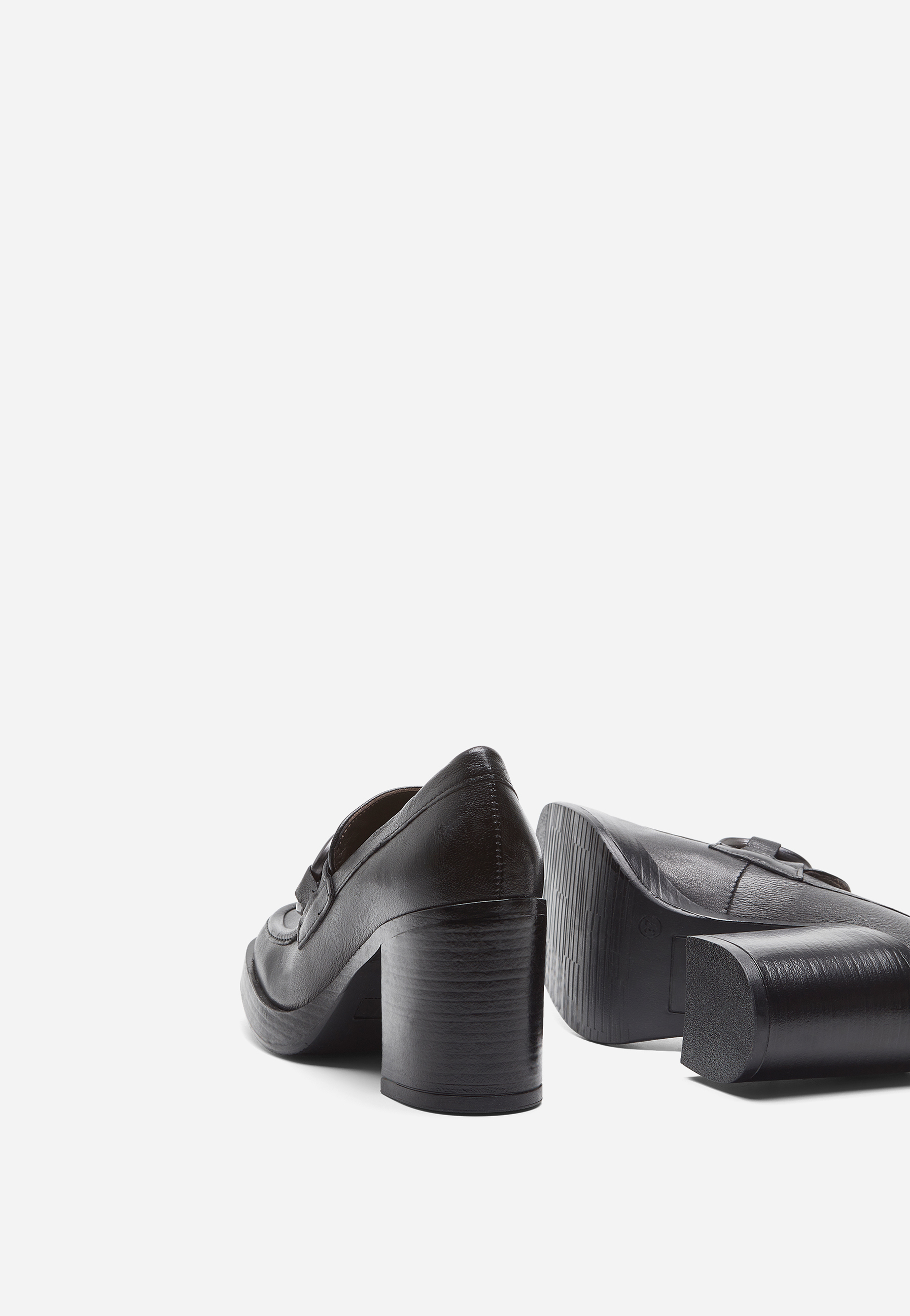 Ein Paar schwarze Halbschuhe mit Absatz, von denen einer aufrecht steht und der andere auf der Seite liegt, vor einem schlichten weißen Hintergrund. Die Schuhe haben einen klobigen Absatz und eine glatte, polierte Textur.