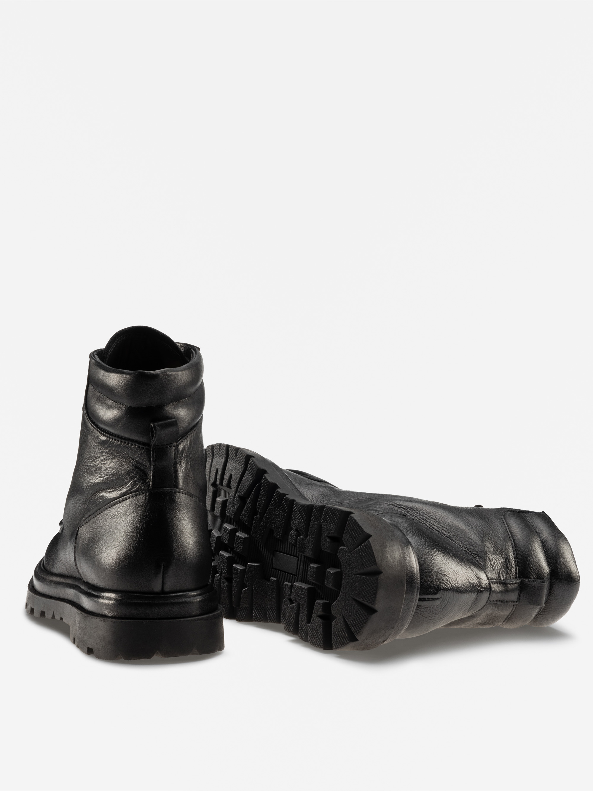 Ein Paar schwarzer Lederstiefel, von denen einer aufrecht steht und der andere auf der Seite liegt, mit einer dicken, robusten Sohle mit tiefem Profil vor einem schlichten weißen Hintergrund.
