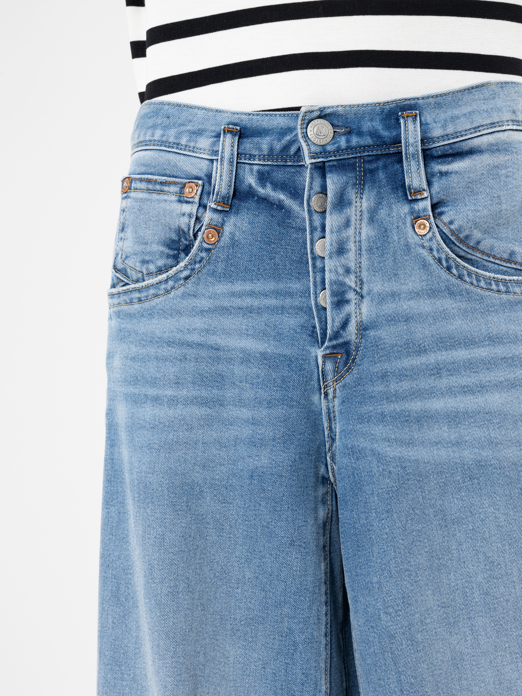 Eine Person trägt eine hellblaue Jeans mit hoher Taille und freiliegenden Knöpfen und ein schwarz-weiß gestreiftes Oberteil. Der Schwerpunkt liegt auf dem Taillen- und Hüftbereich der Jeans.