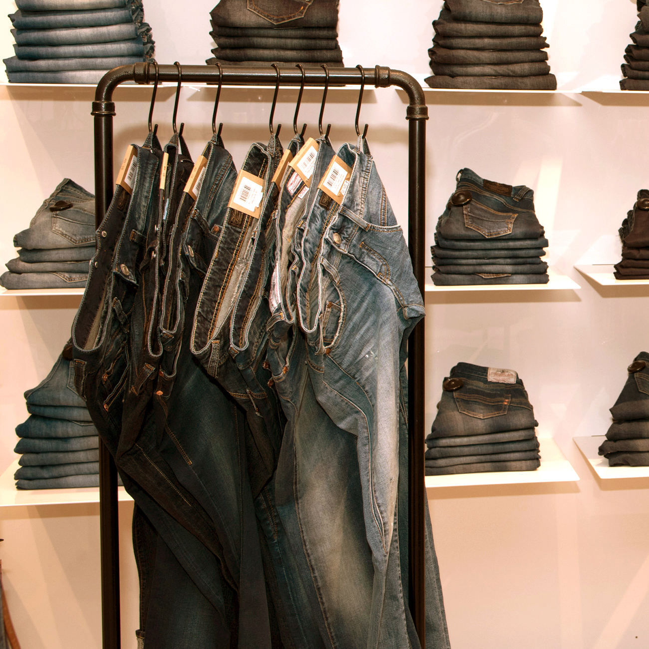 Ein Bekleidungsgeschäft mit mehreren blauen Jeans, die auf einem Gestell im Vordergrund hängen, und ordentlich gefalteten Jeans, die auf weißen Regalen im Hintergrund gestapelt sind.
