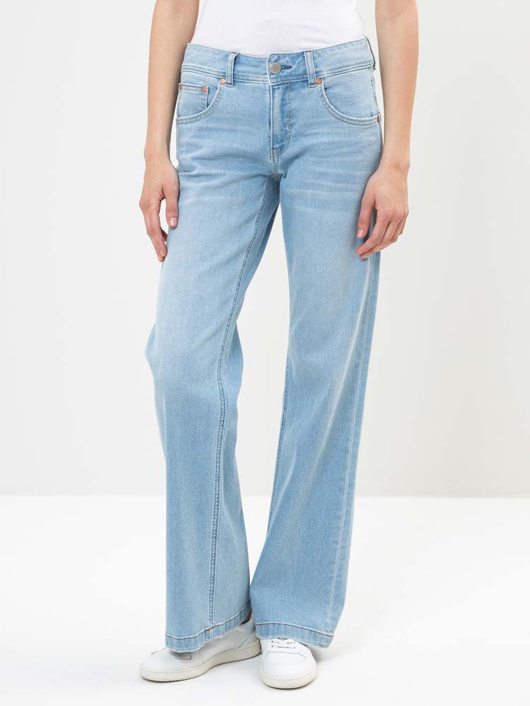 Eine Person, die hellblaue, weit geschnittene Jeans, ein weißes Oberteil und weiße Turnschuhe trägt, steht vor einem schlichten weißen Hintergrund. Das Foto zeigt die Jeans von der Taille bis zu den Füßen.