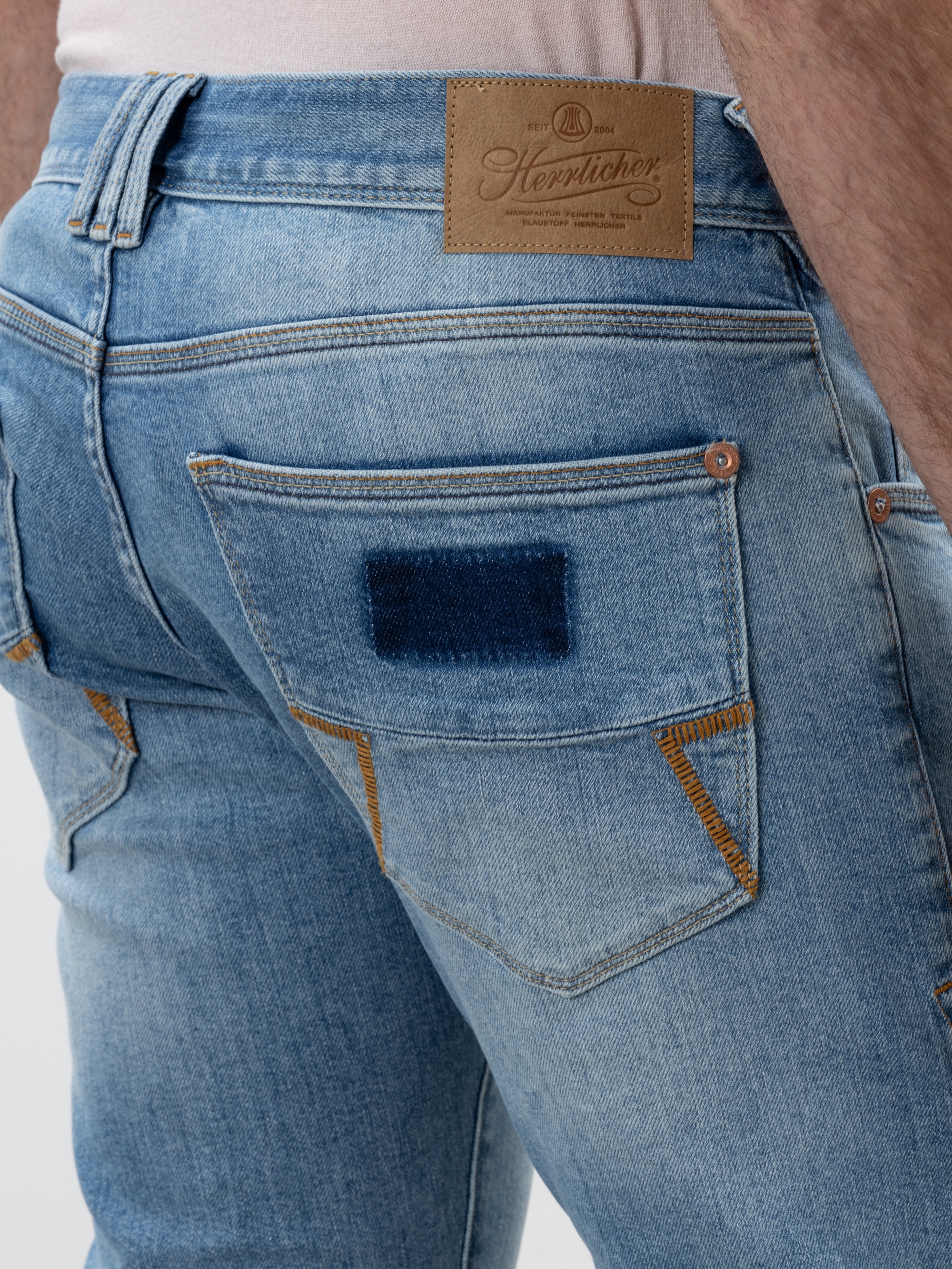 Nahaufnahme des Rückens einer Person, die eine hellblaue Jeans mit einem braunen Markenaufnäher aus Leder und einem dunkelblauen rechteckigen Aufnäher auf der rechten Gesäßtasche trägt.